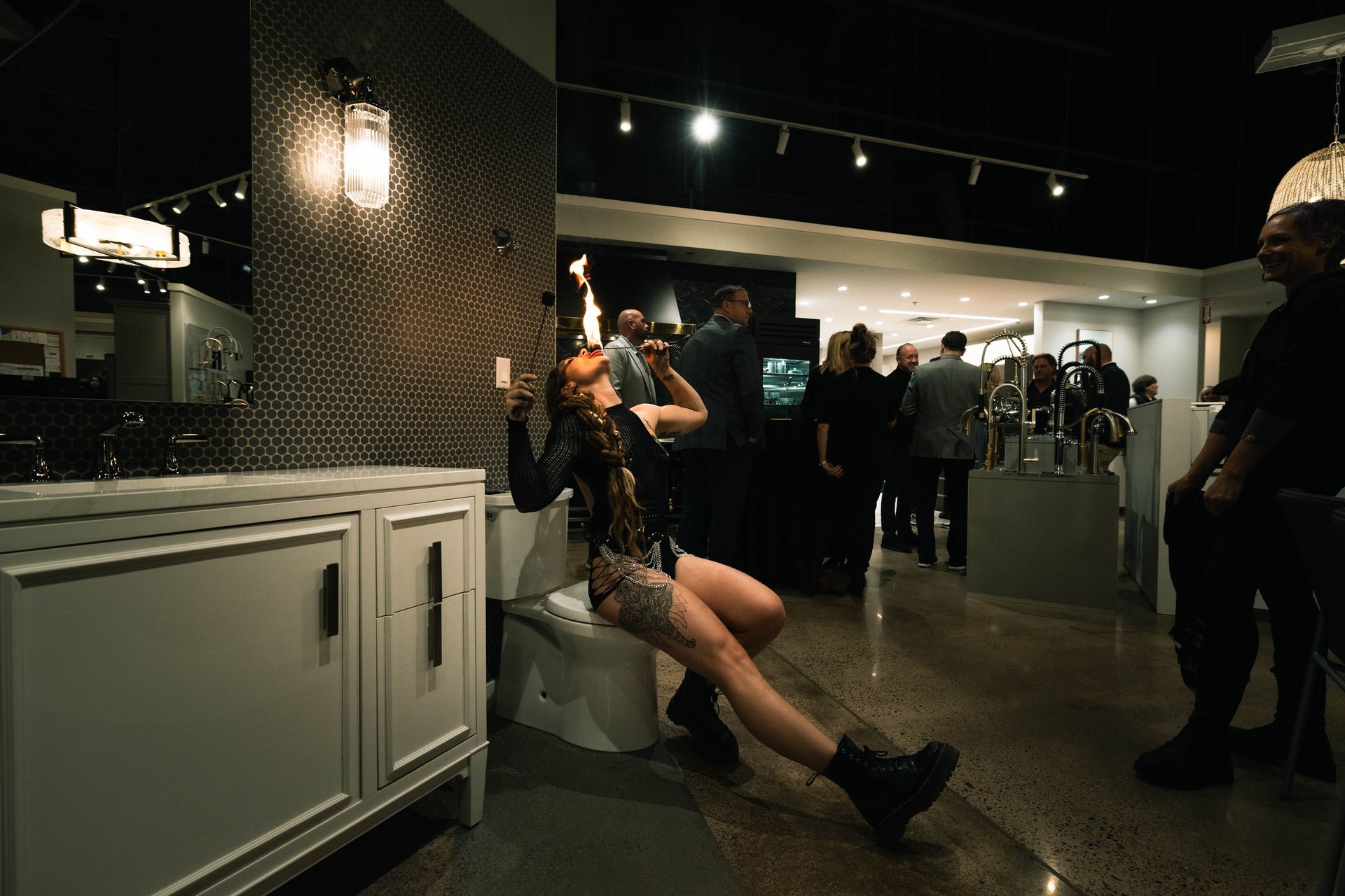 A woman eating fire while sitting a toilet in the middle of a showroom.