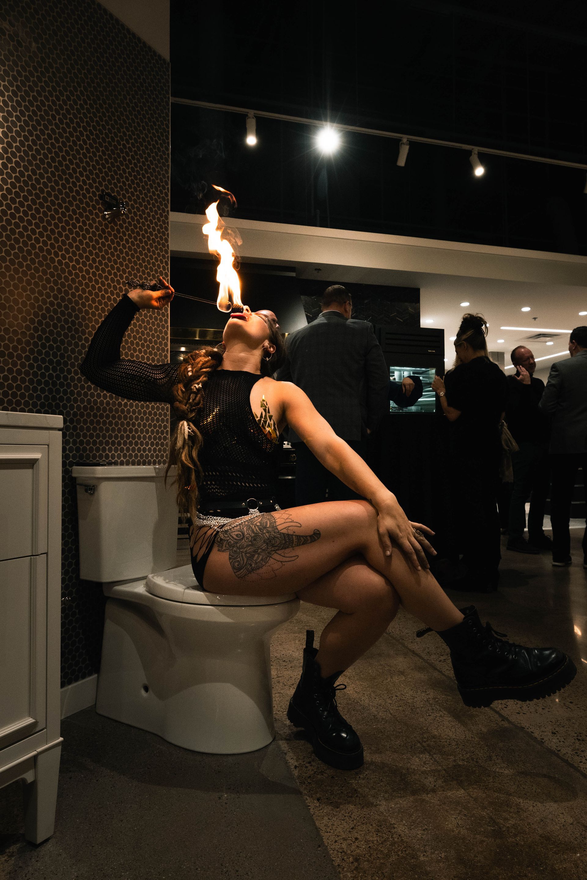A woman performing with fire while sitting on a toilet inside a showroom.