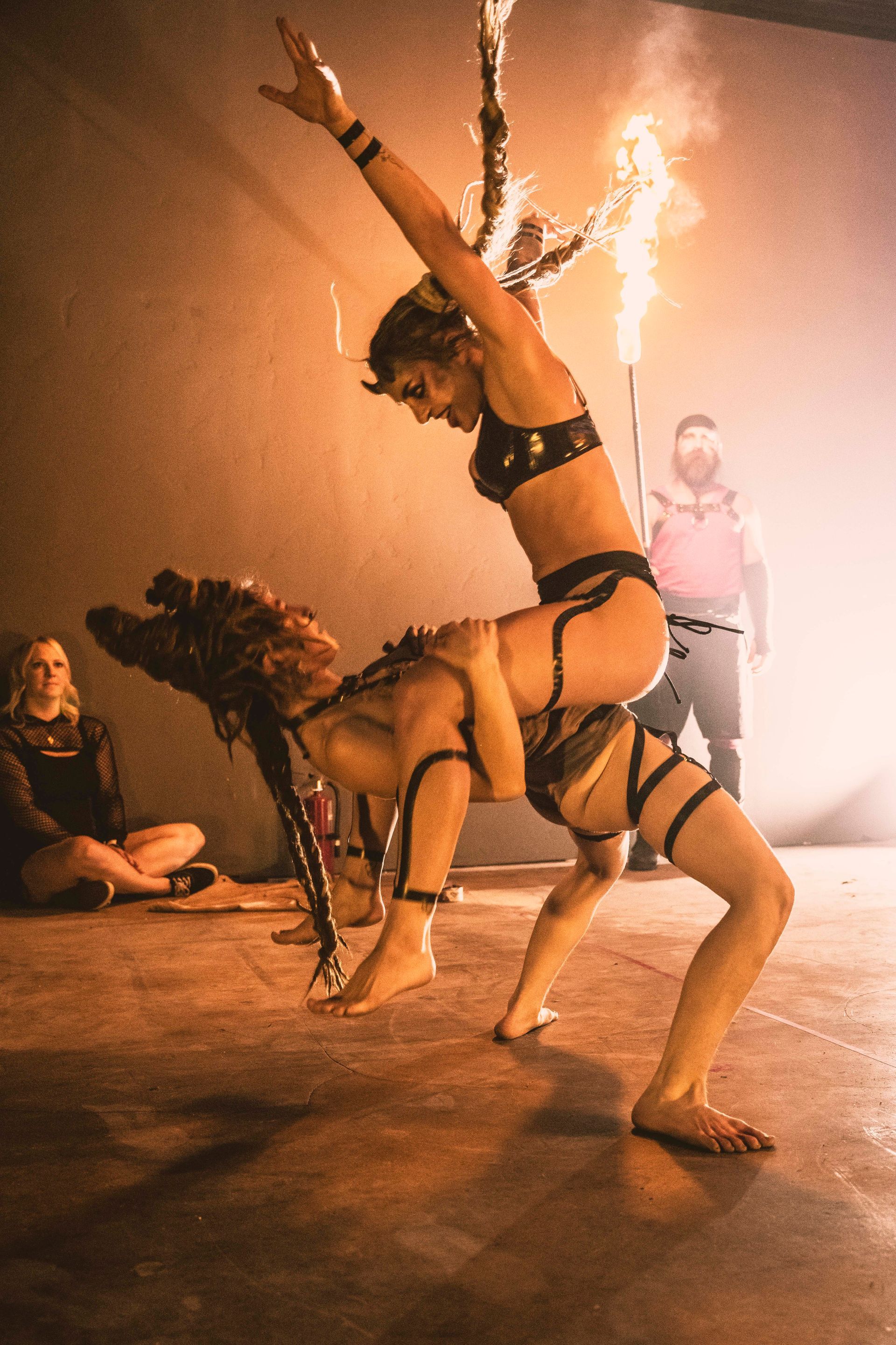 Two female performers on stage with one sitting on the other.