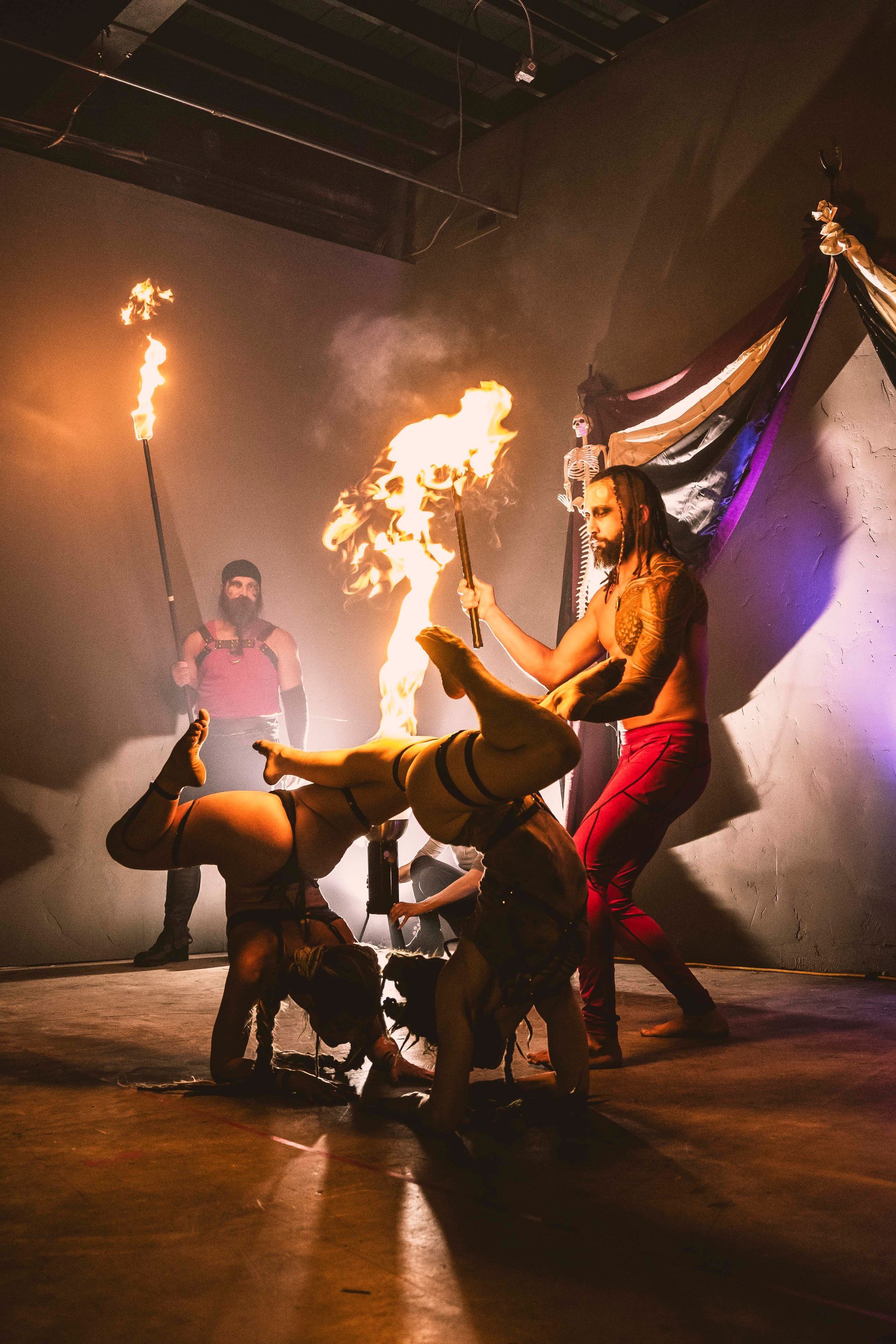 A man lighting two woman on fire for a fire show safely.