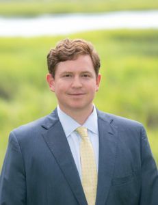 A man in a suit and tie is standing in front of a field.