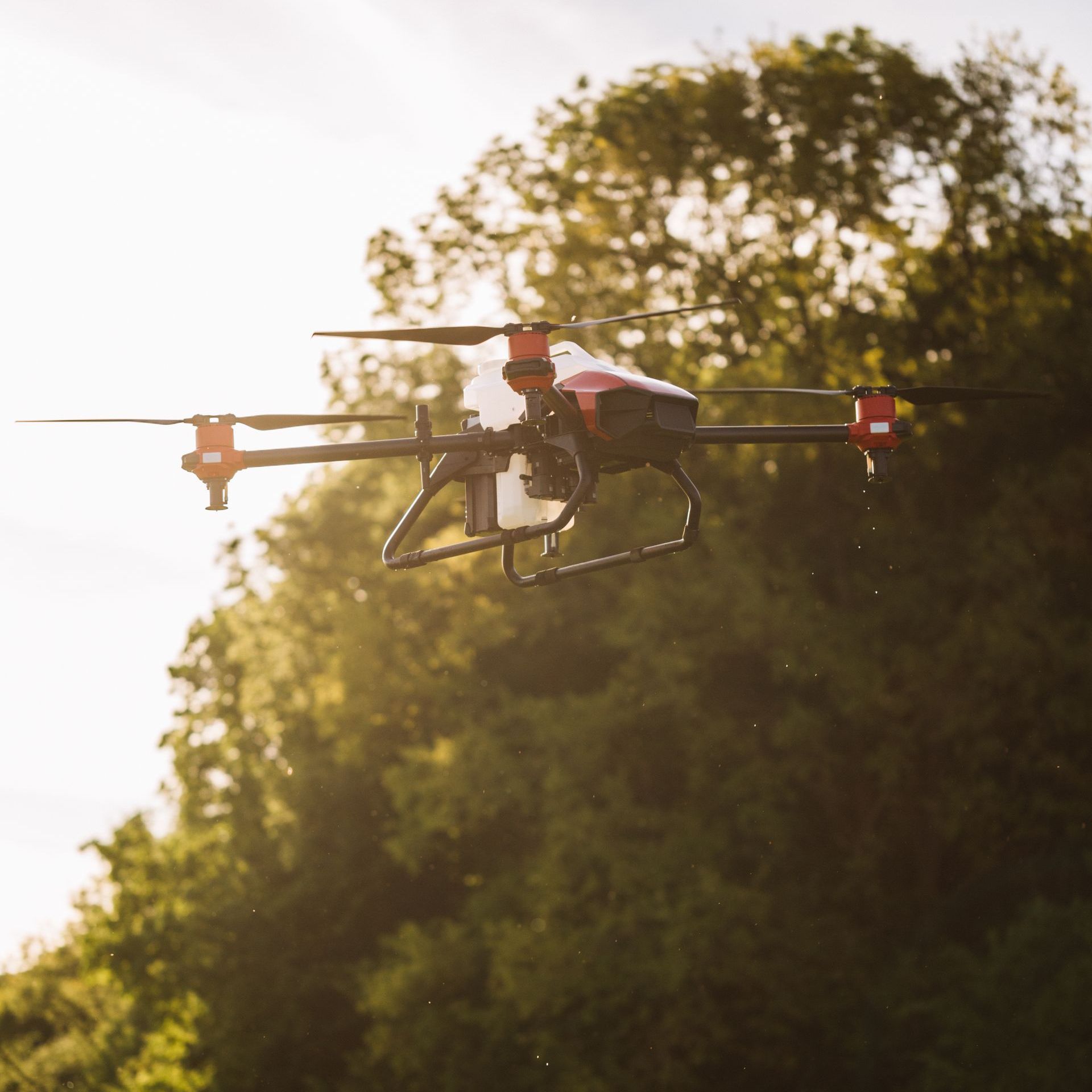 A red drone is flying in the sky over a field