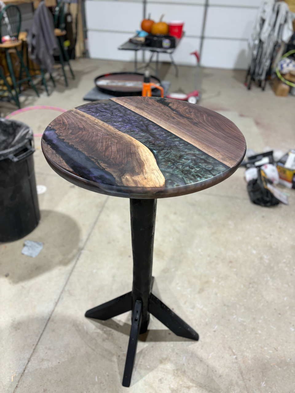 A round table with a black base and a live edge wooden top that showcases an epoxy inlay