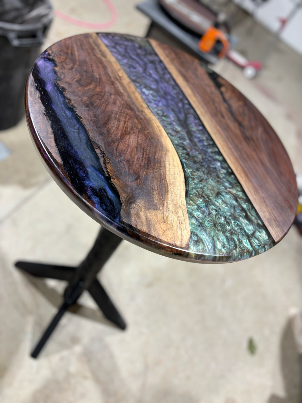 A round table with a black base and a live edge wooden top that showcases an epoxy inlay