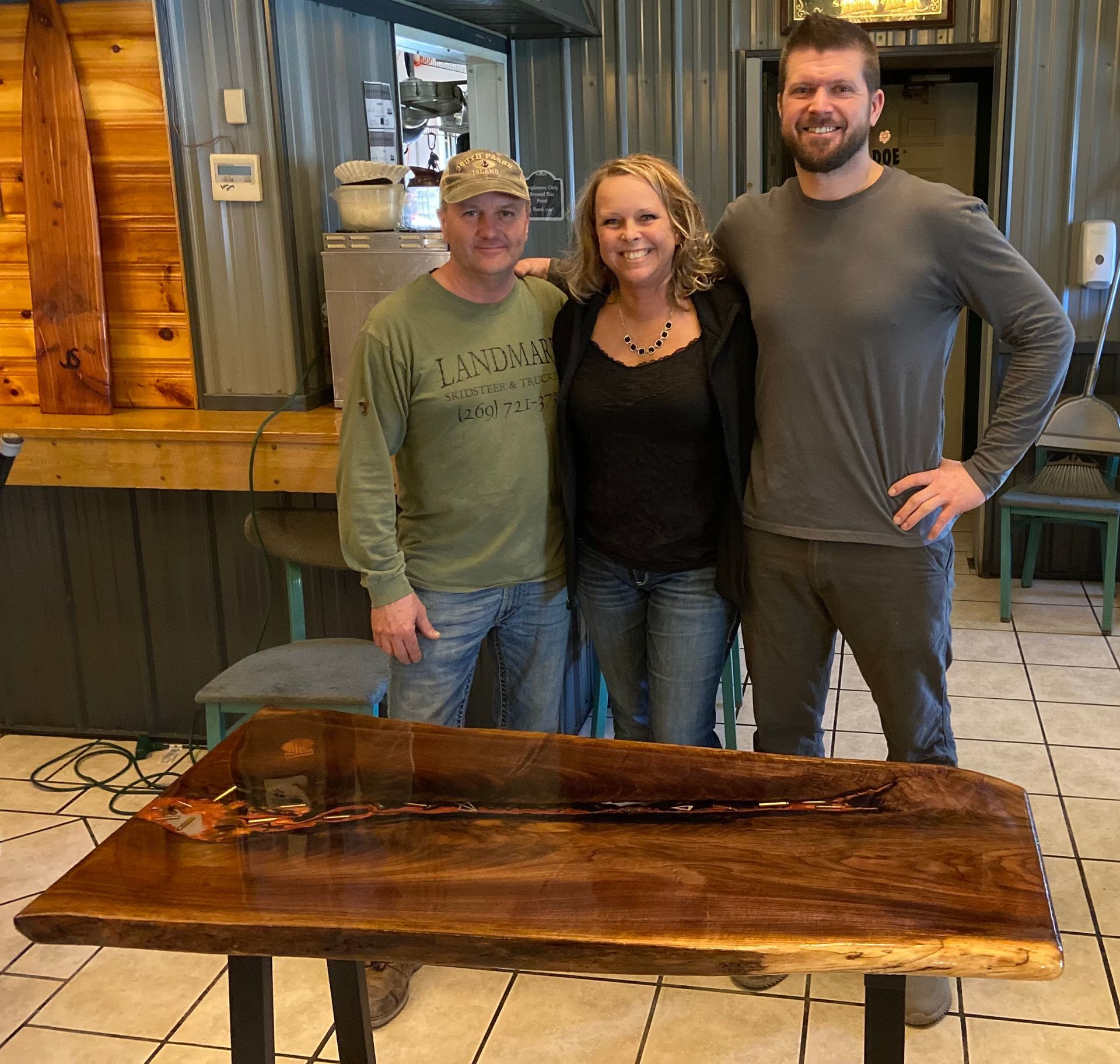 Three people are posing for a picture in front of a wooden table made by Timmberman's Woodworking
