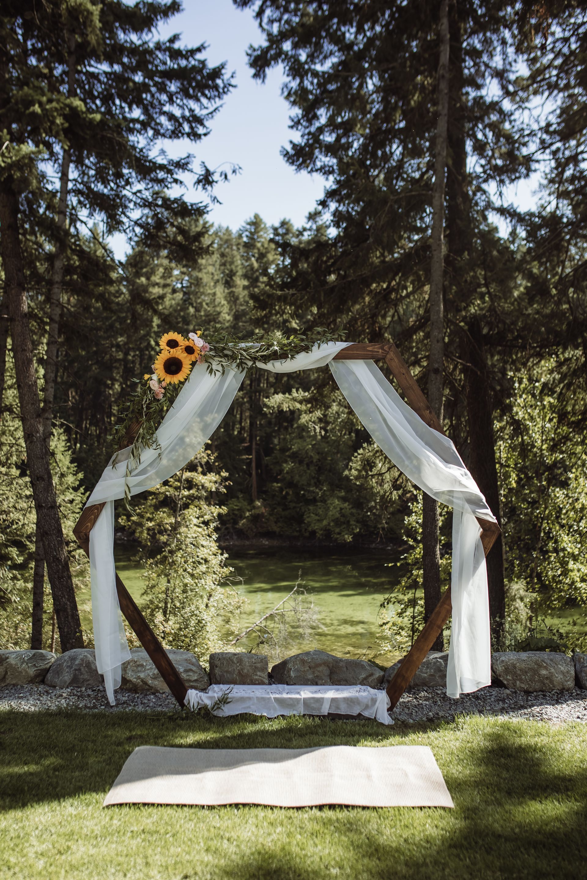 A wedding arch in the middle of a forest with a sunflower on top.