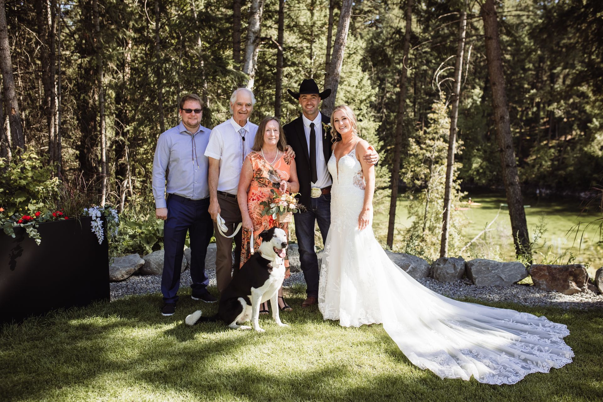 A bride and groom are posing for a picture with their family and their dog.