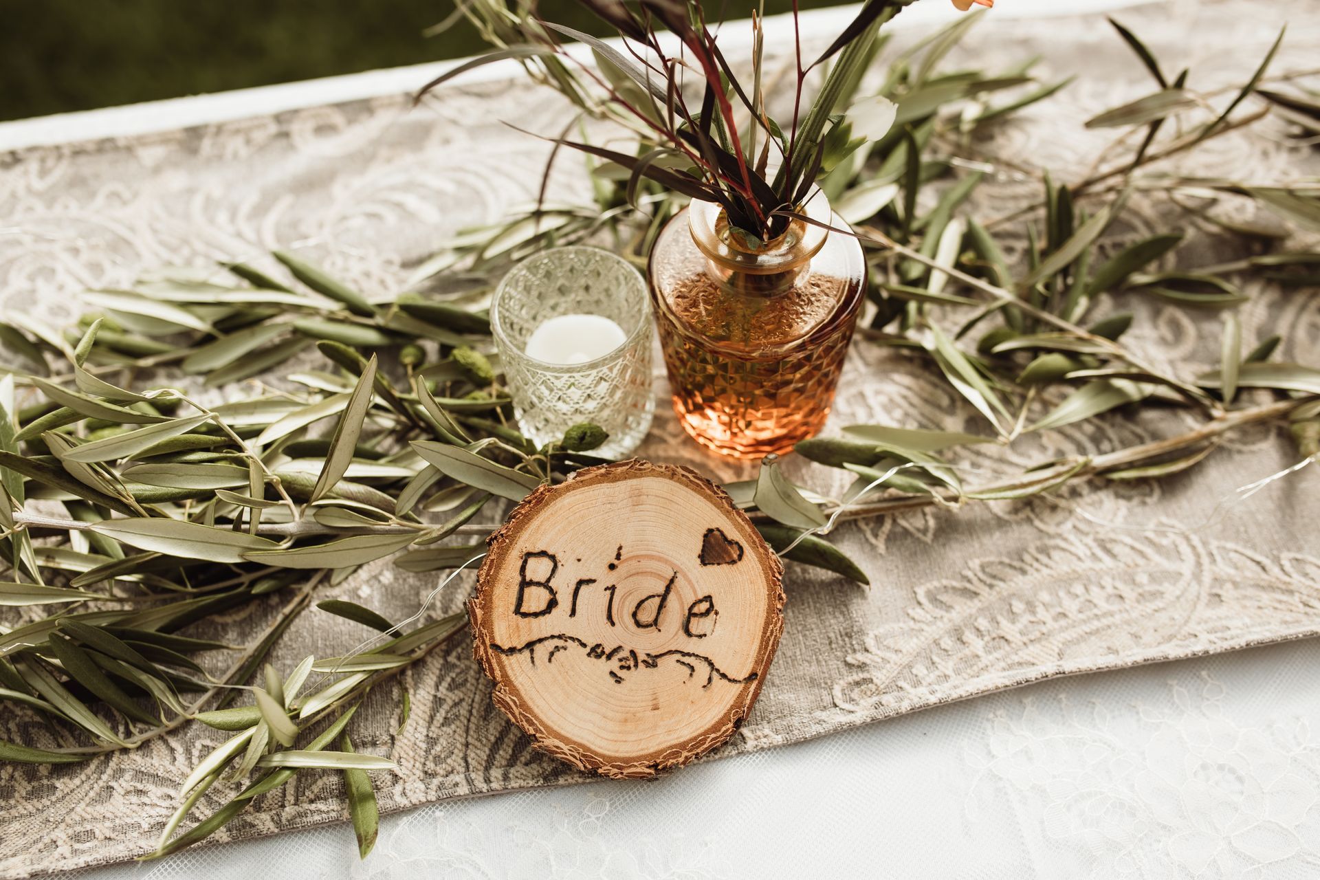 A wooden sign that says `` bride '' is sitting on a table next to a vase of flowers.