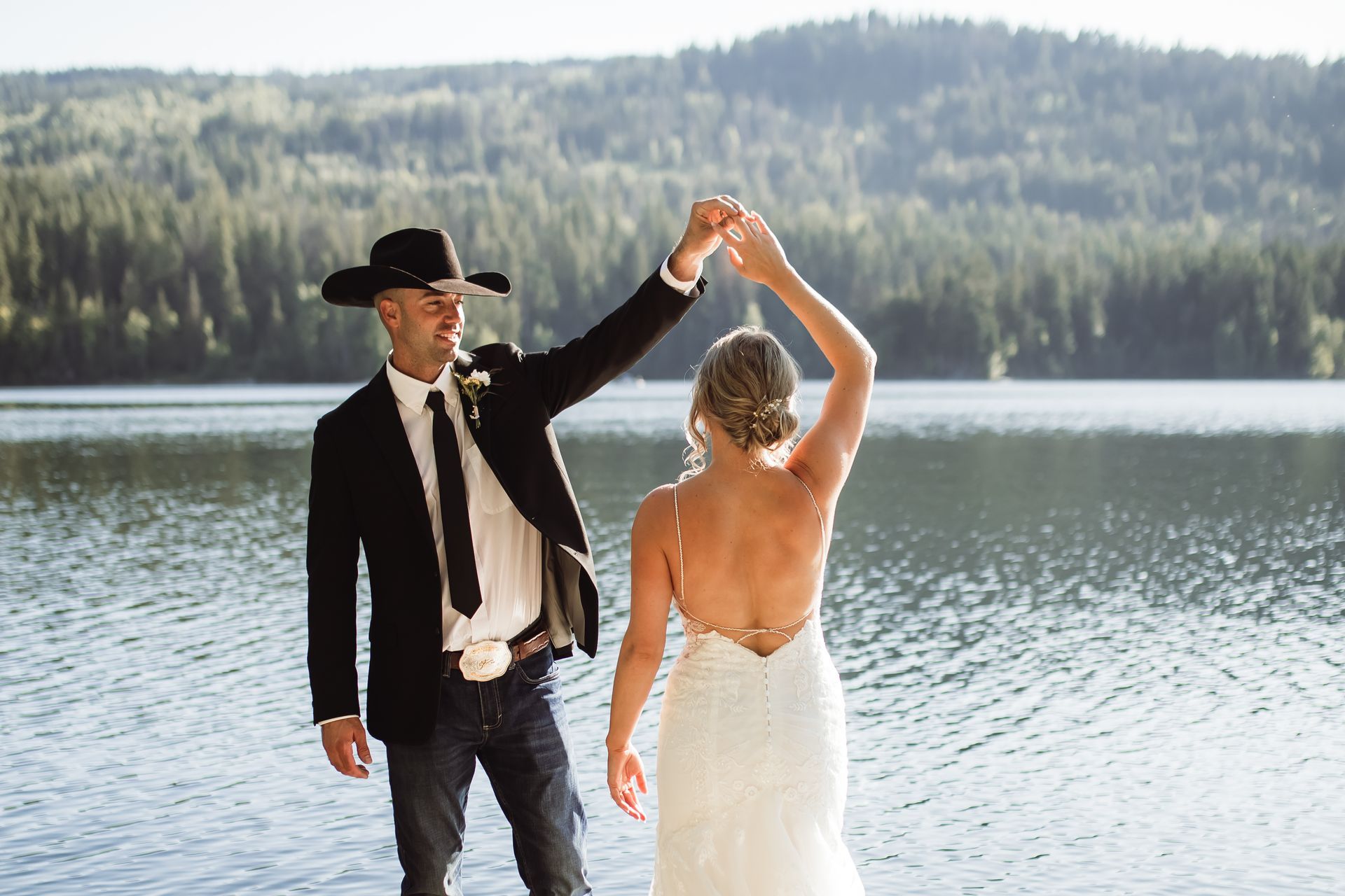 A bride and groom are dancing on the shore of a lake.