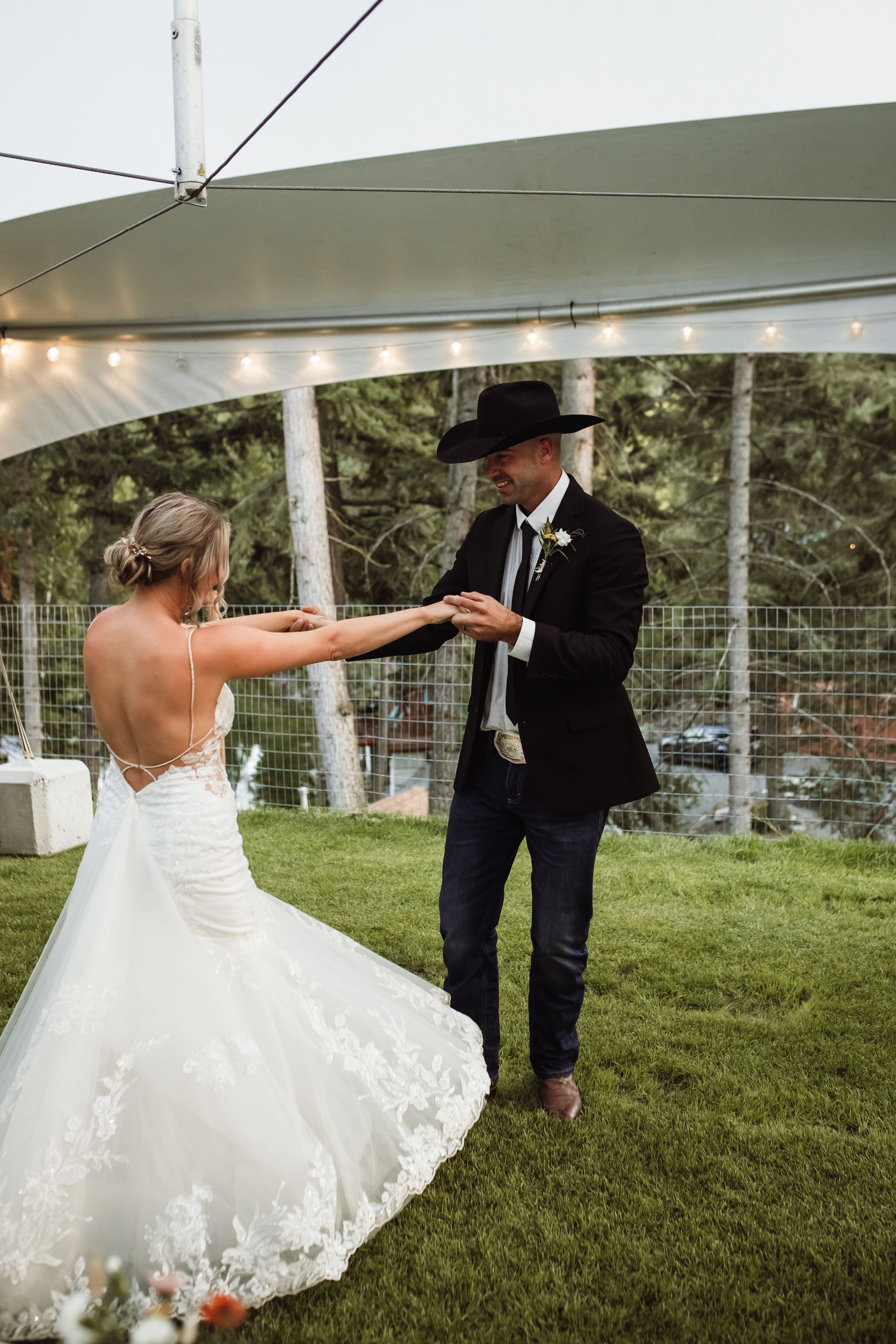 A bride and groom are dancing under a tent in the grass.