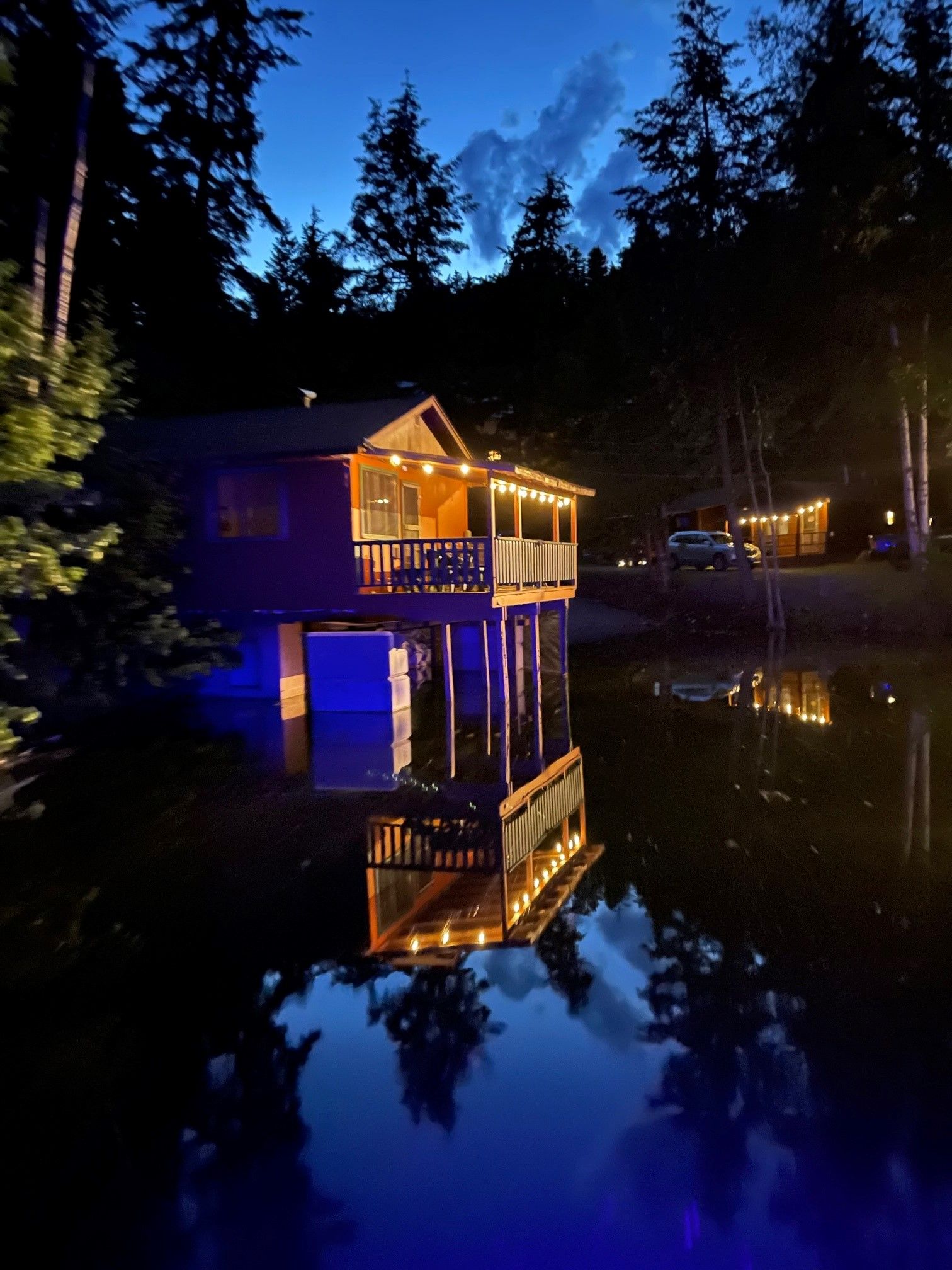 A house on stilts is lit up at night and is reflected in the water.