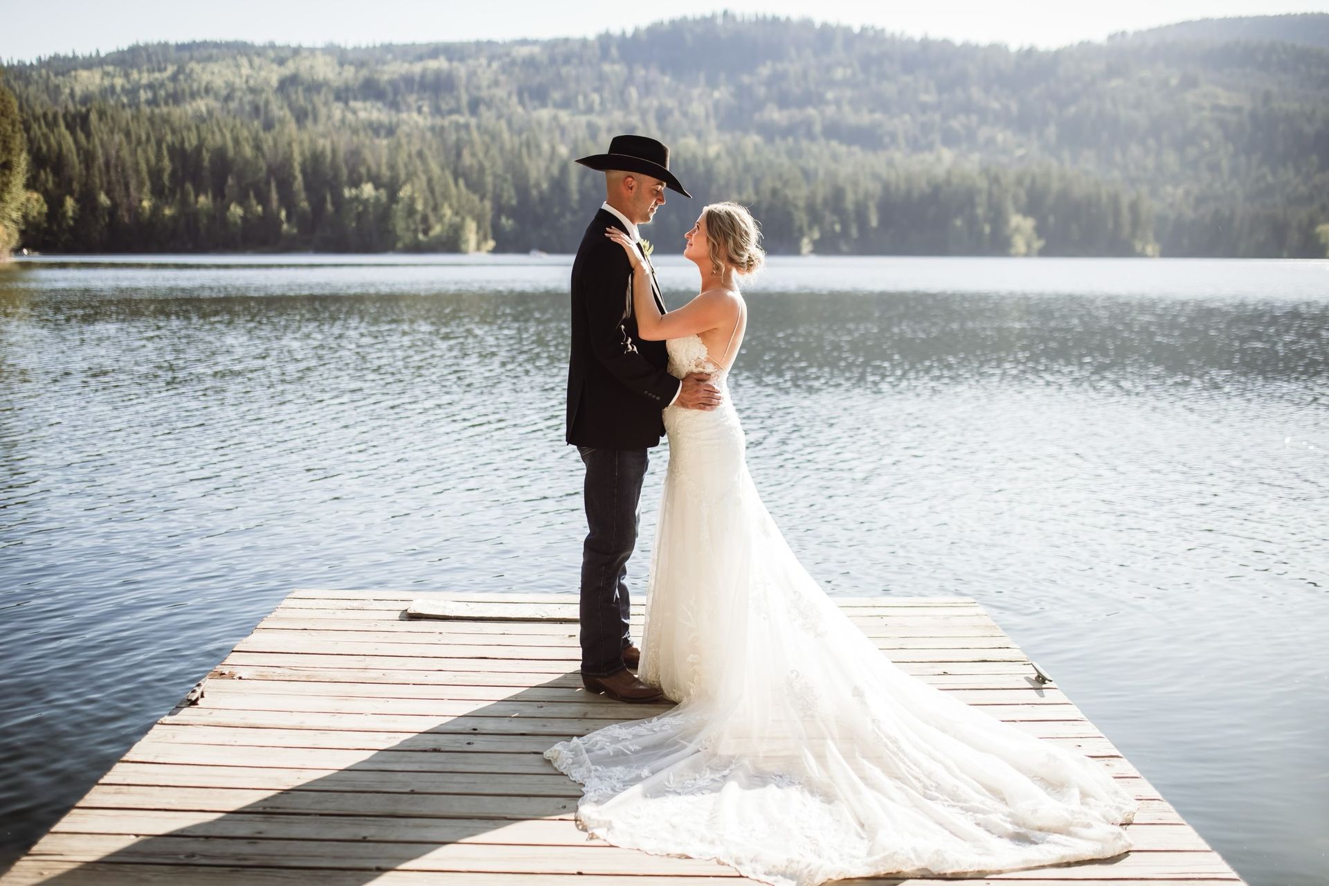 A bride and groom are standing on a dock next to a lake.