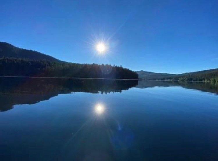 The sun is reflected in the water of a lake surrounded by mountains.