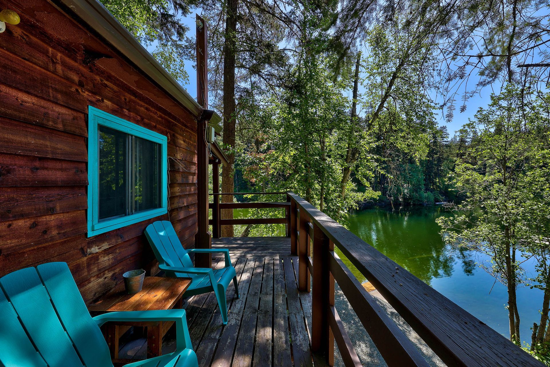 A wooden cabin with blue chairs on a deck overlooking a lake