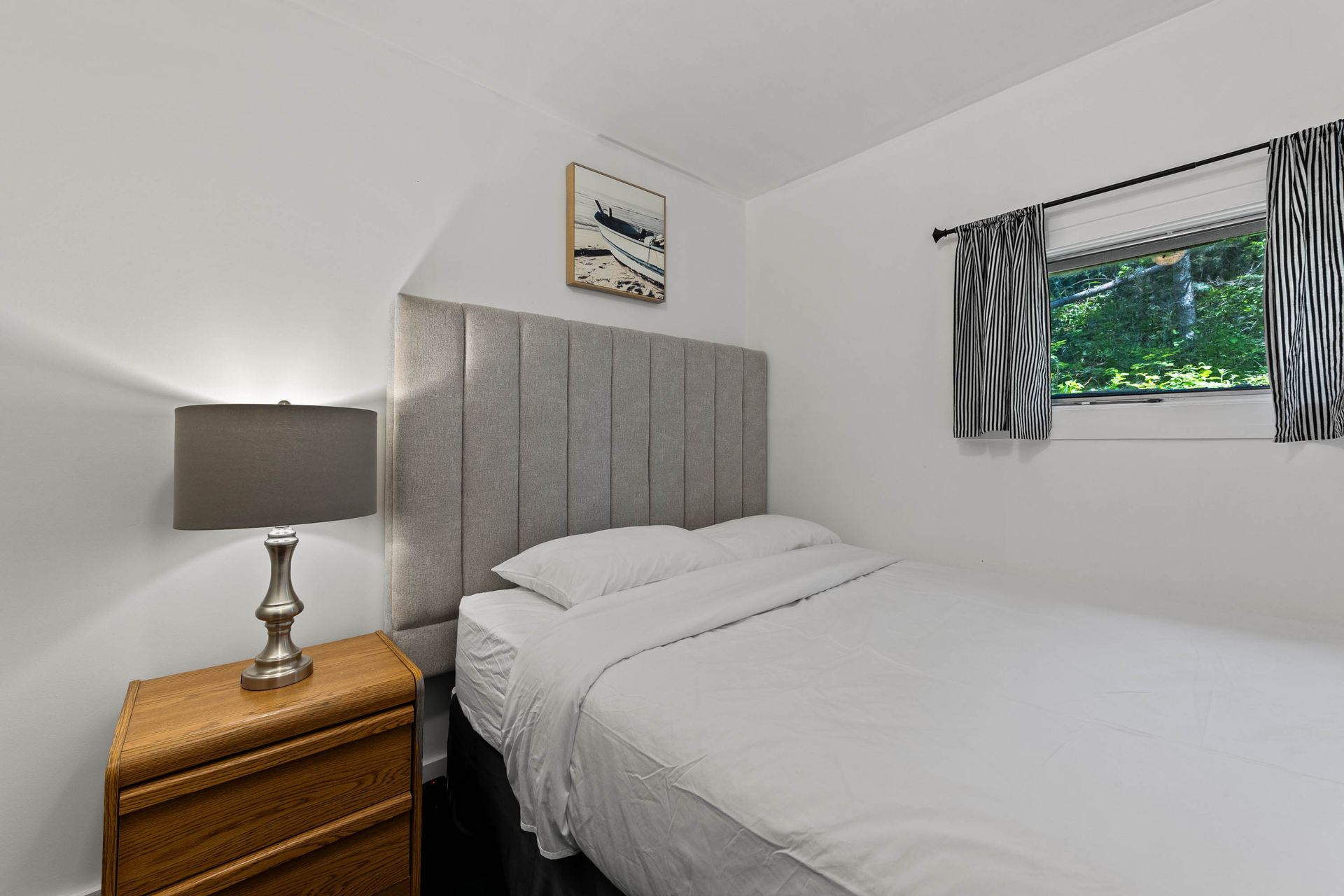 A bedroom with a bed , nightstand , lamp and window.