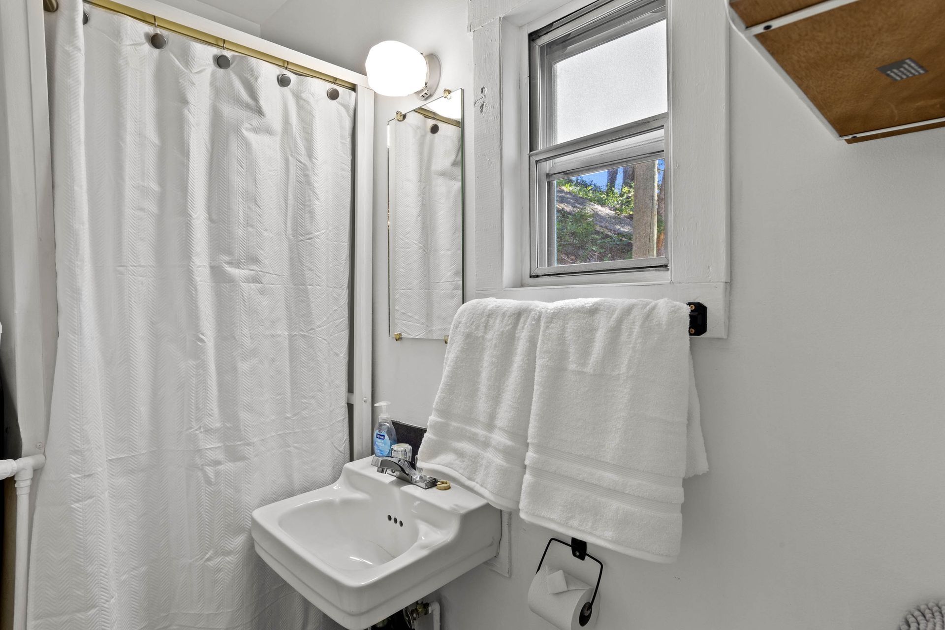 A bathroom with a sink , shower curtain , mirror and window.
