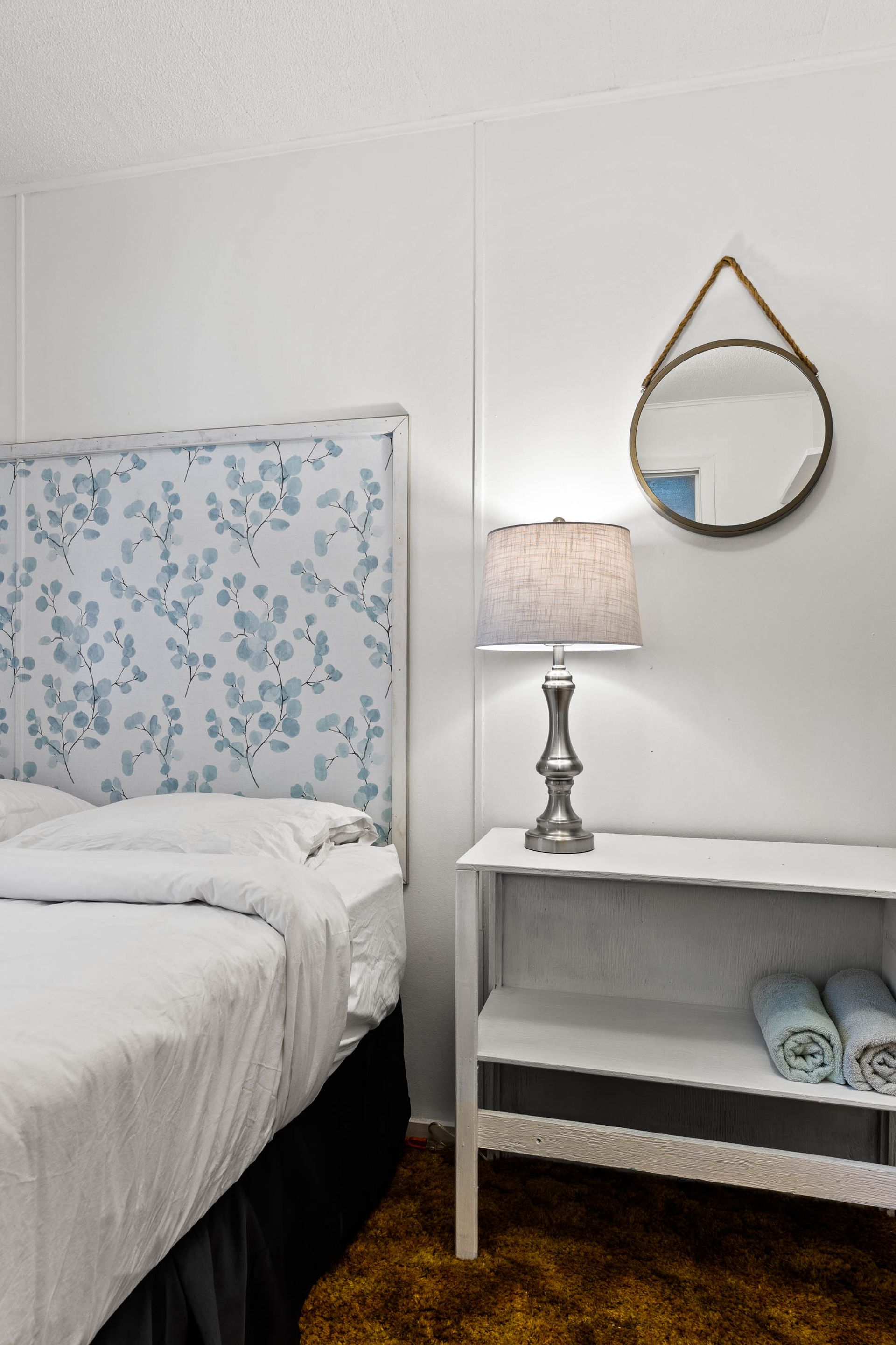 A bedroom with a bed , nightstand , lamp and mirror.