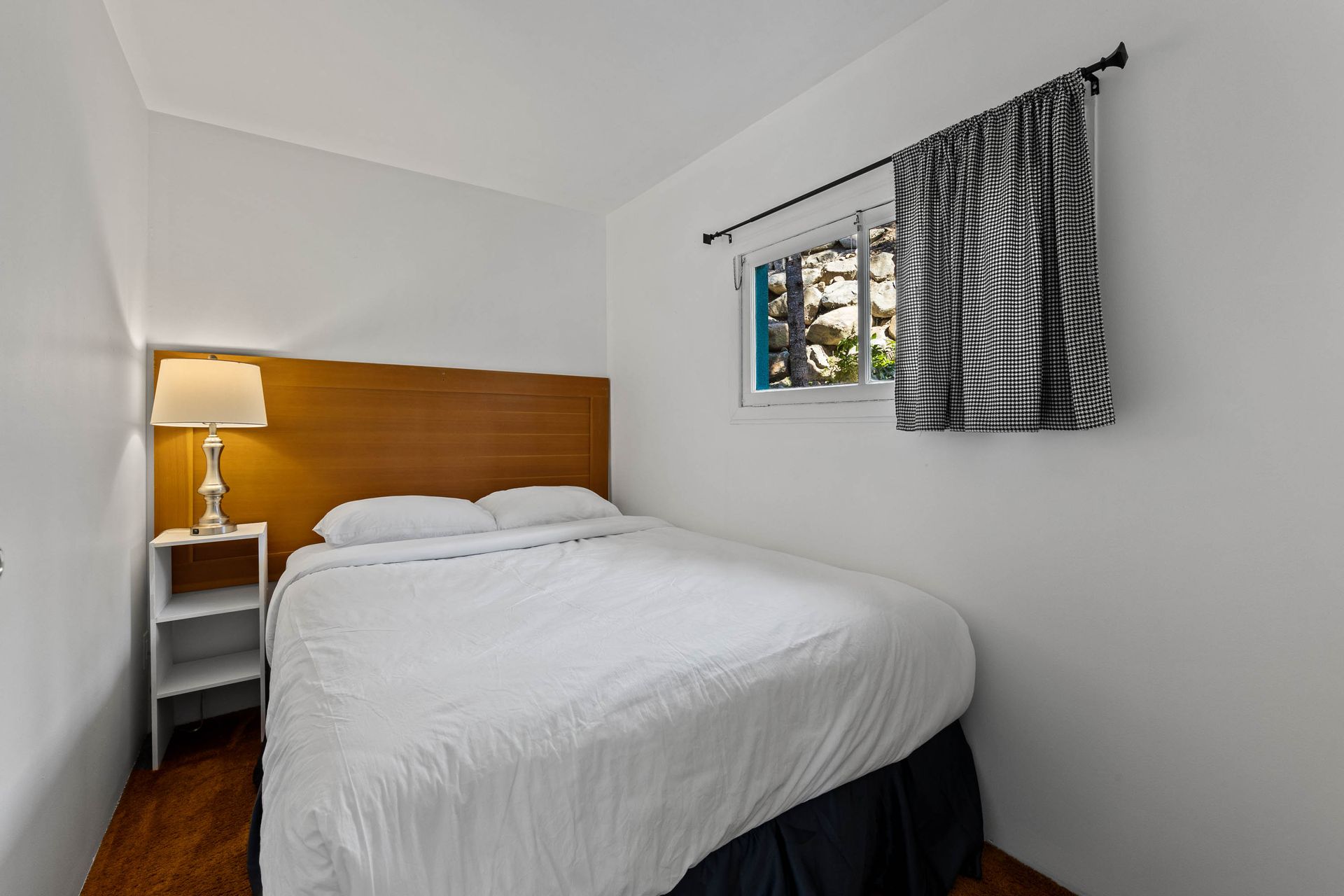 A bedroom with a bed , nightstand , lamp and window.