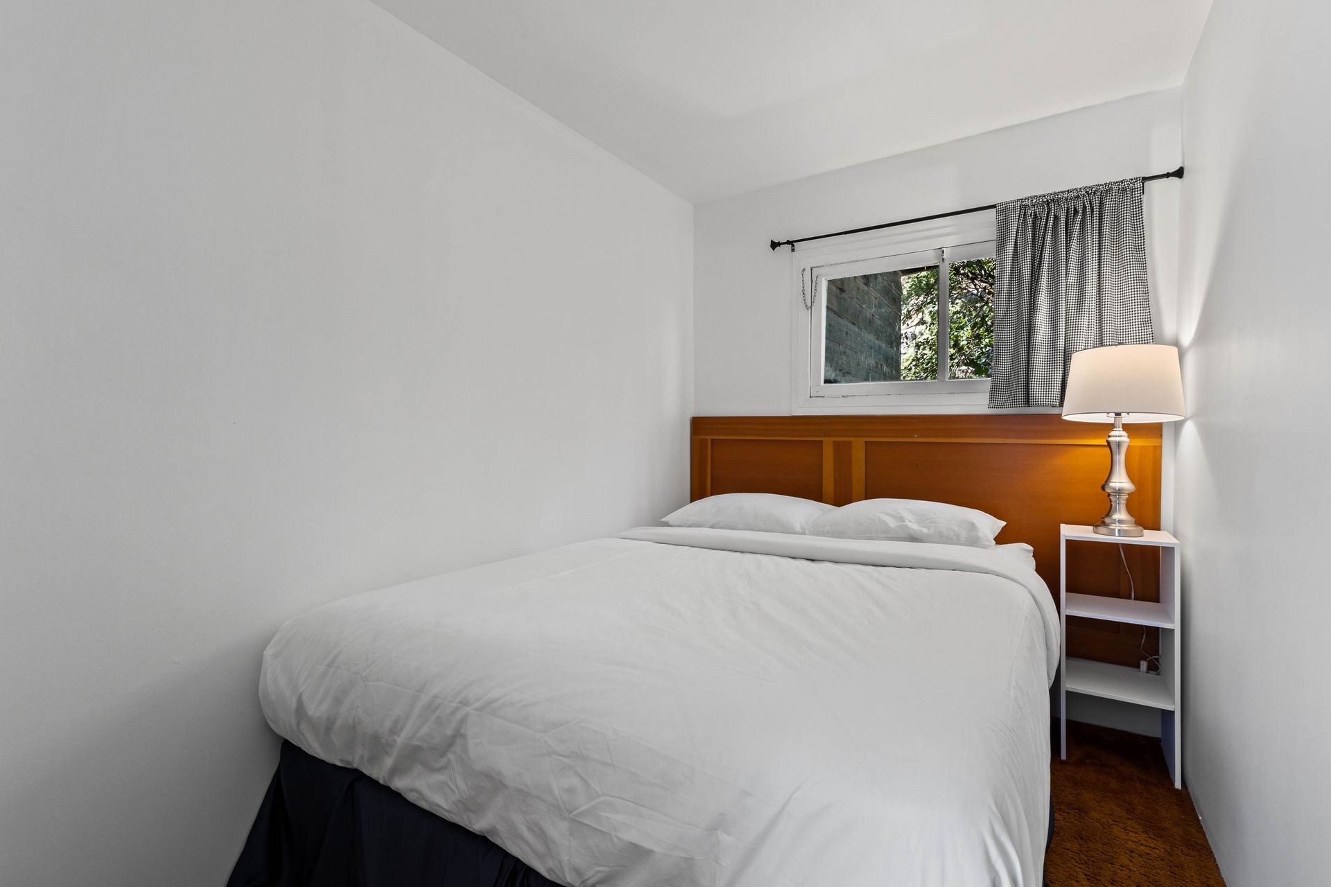 A bedroom with a bed , nightstand , lamp and window.