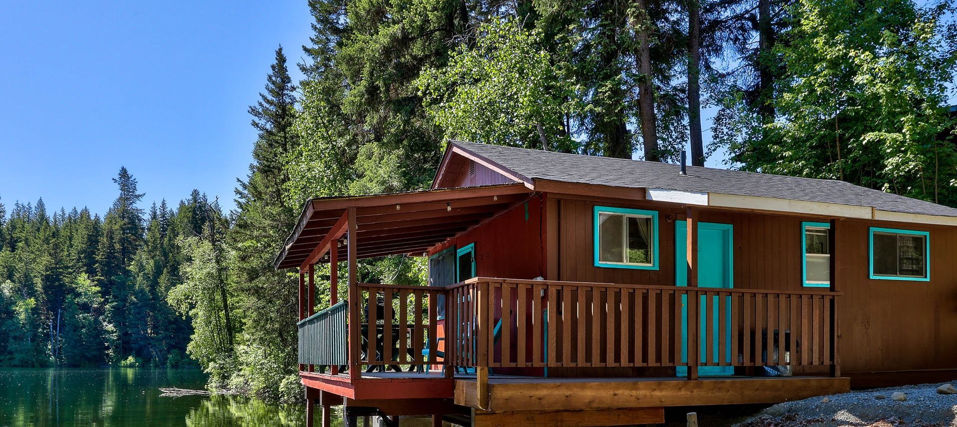 A small house with a deck is sitting on the shore of a lake surrounded by trees.