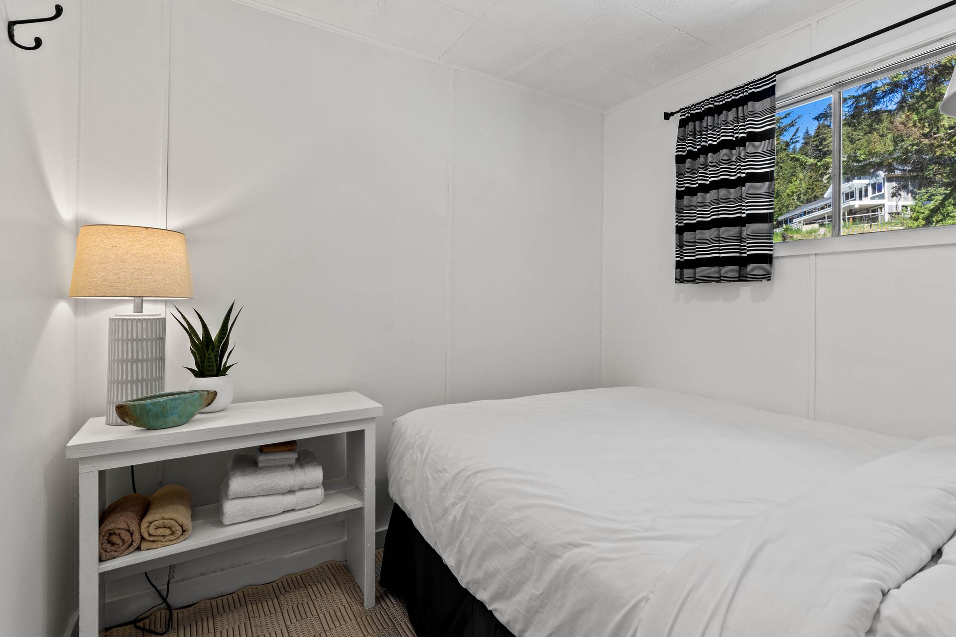 A bedroom with a bed , nightstand , lamp and window.