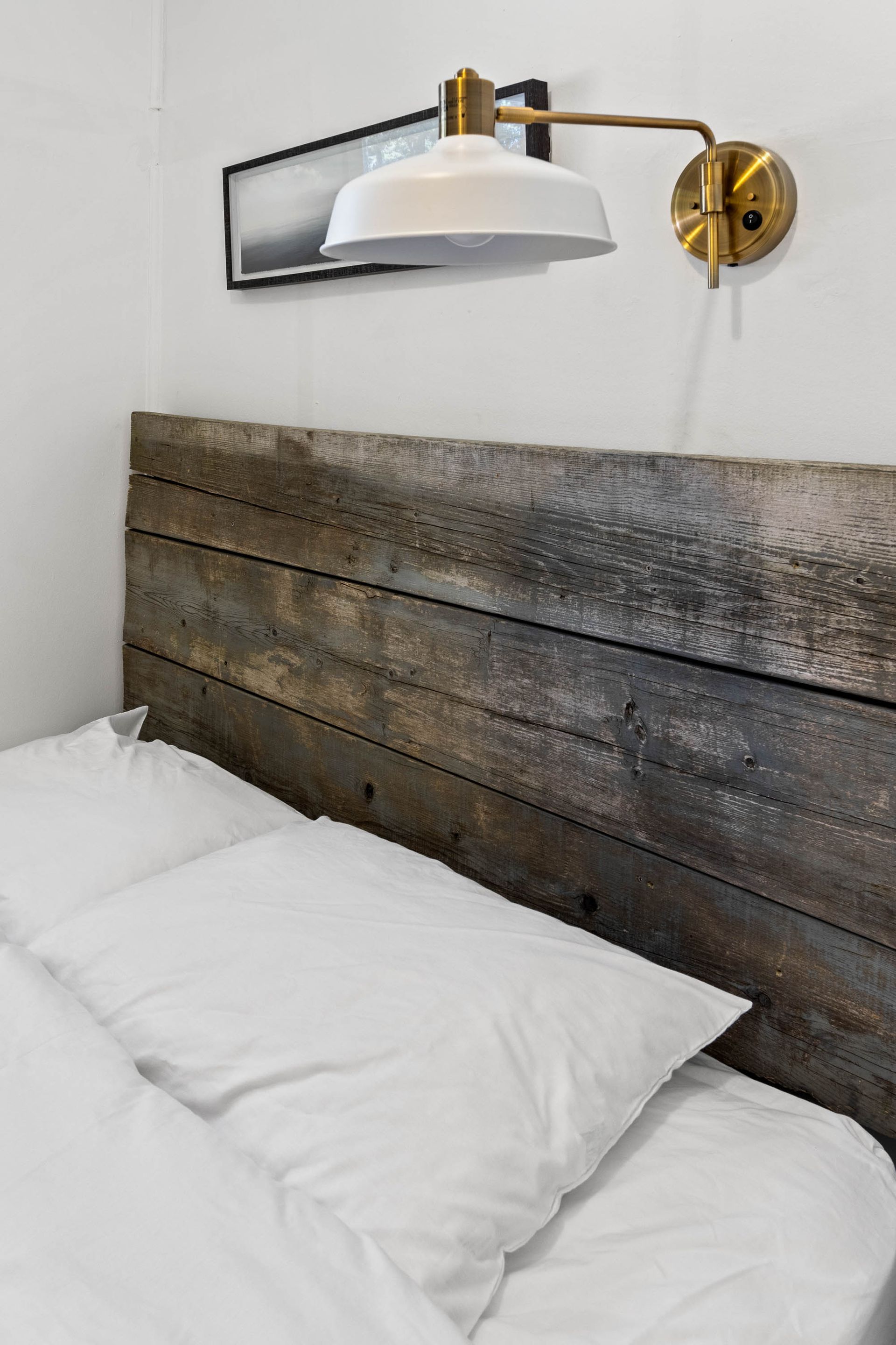 A bed with a wooden headboard and a lamp on the wall.