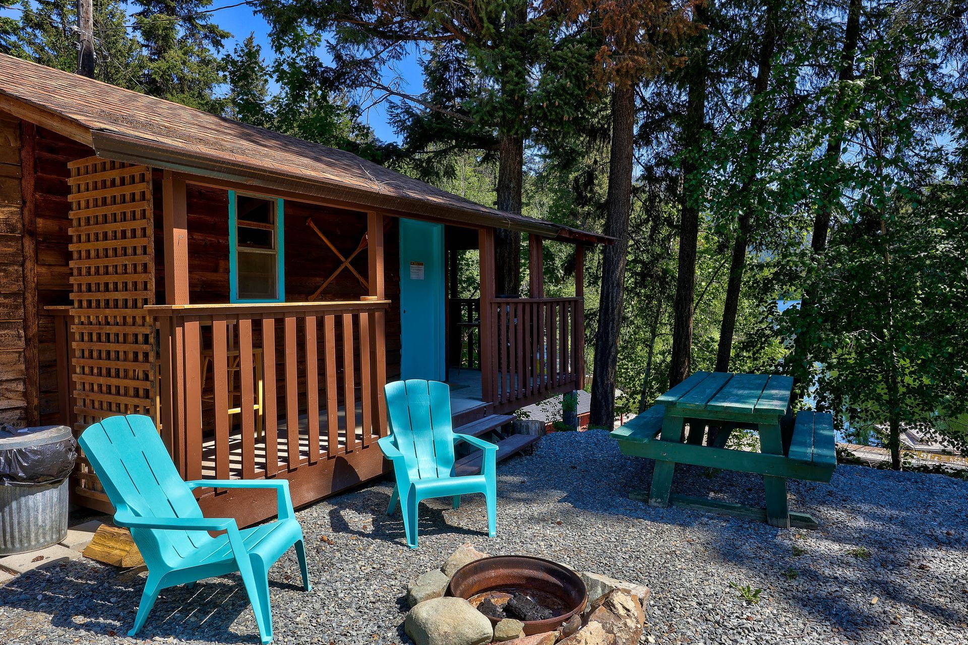 A log cabin with blue chairs and a fire pit in front of it.