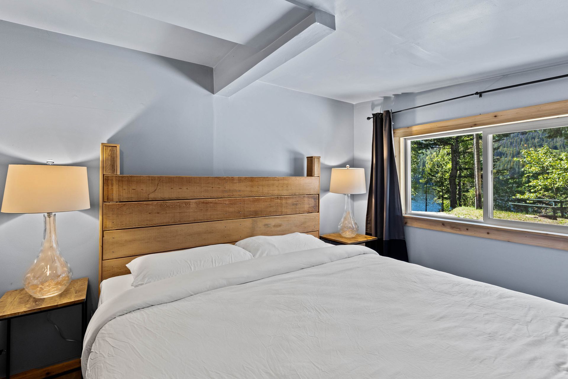 A bedroom with a king size bed , two lamps , and a large window.