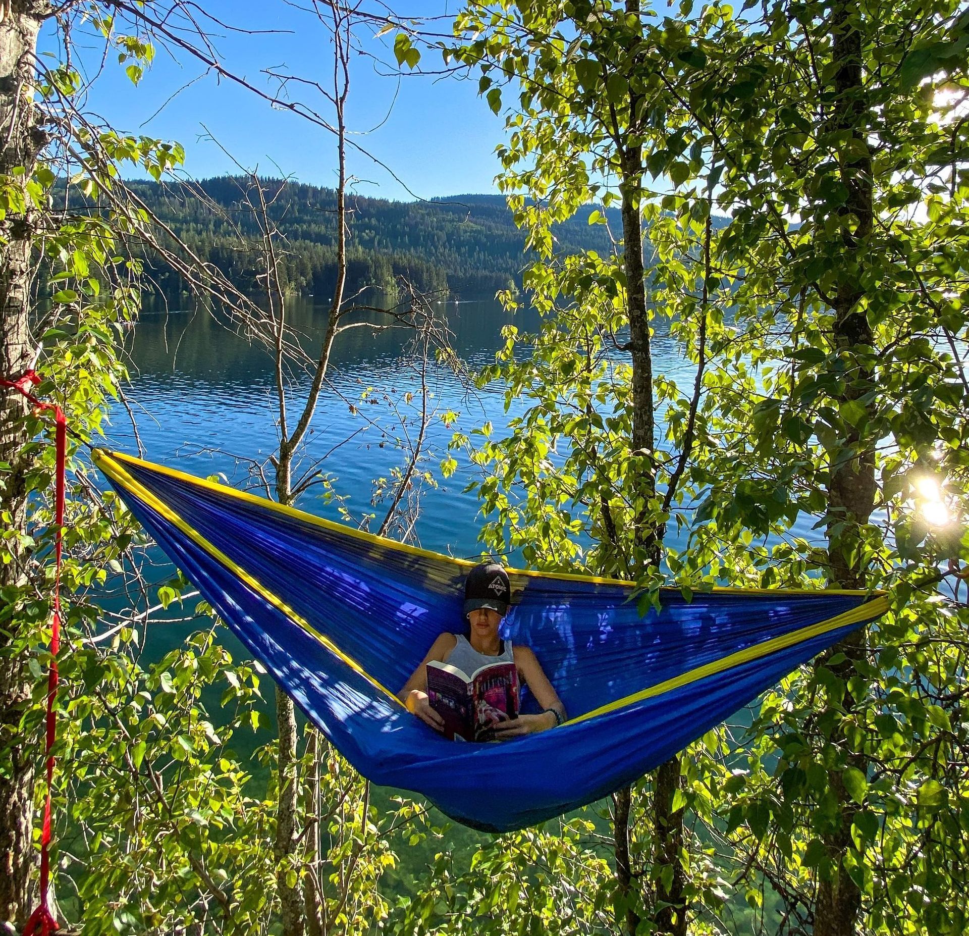A woman is laying in a blue hammock reading a book