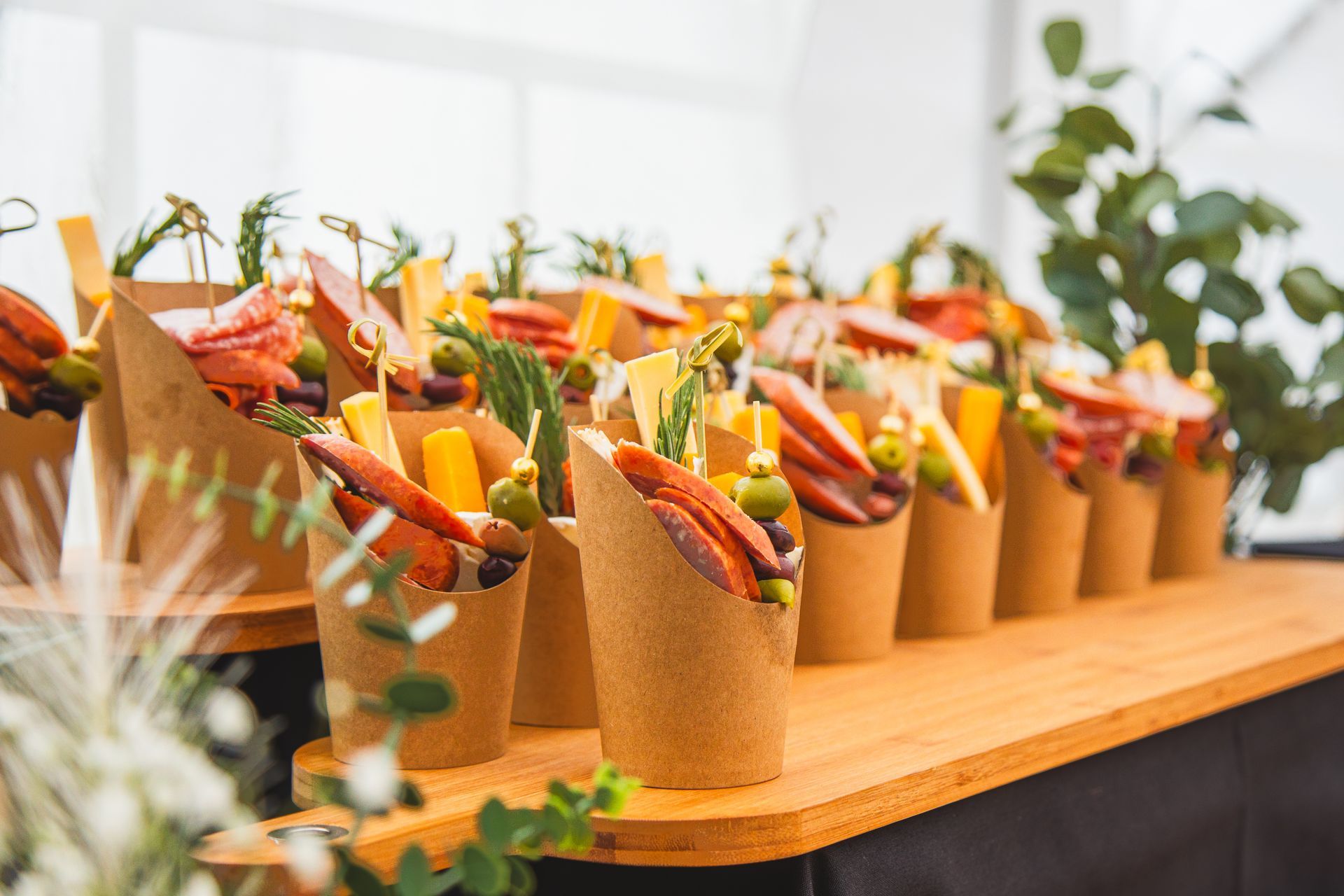 A wooden table topped with a row of paper cups filled with food.