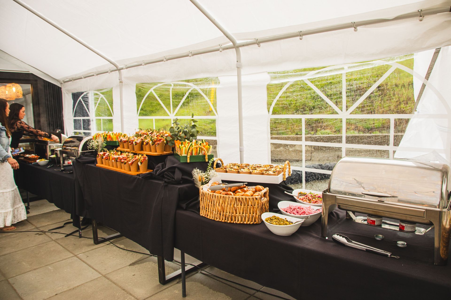 A woman is standing in front of a buffet table under a tent.