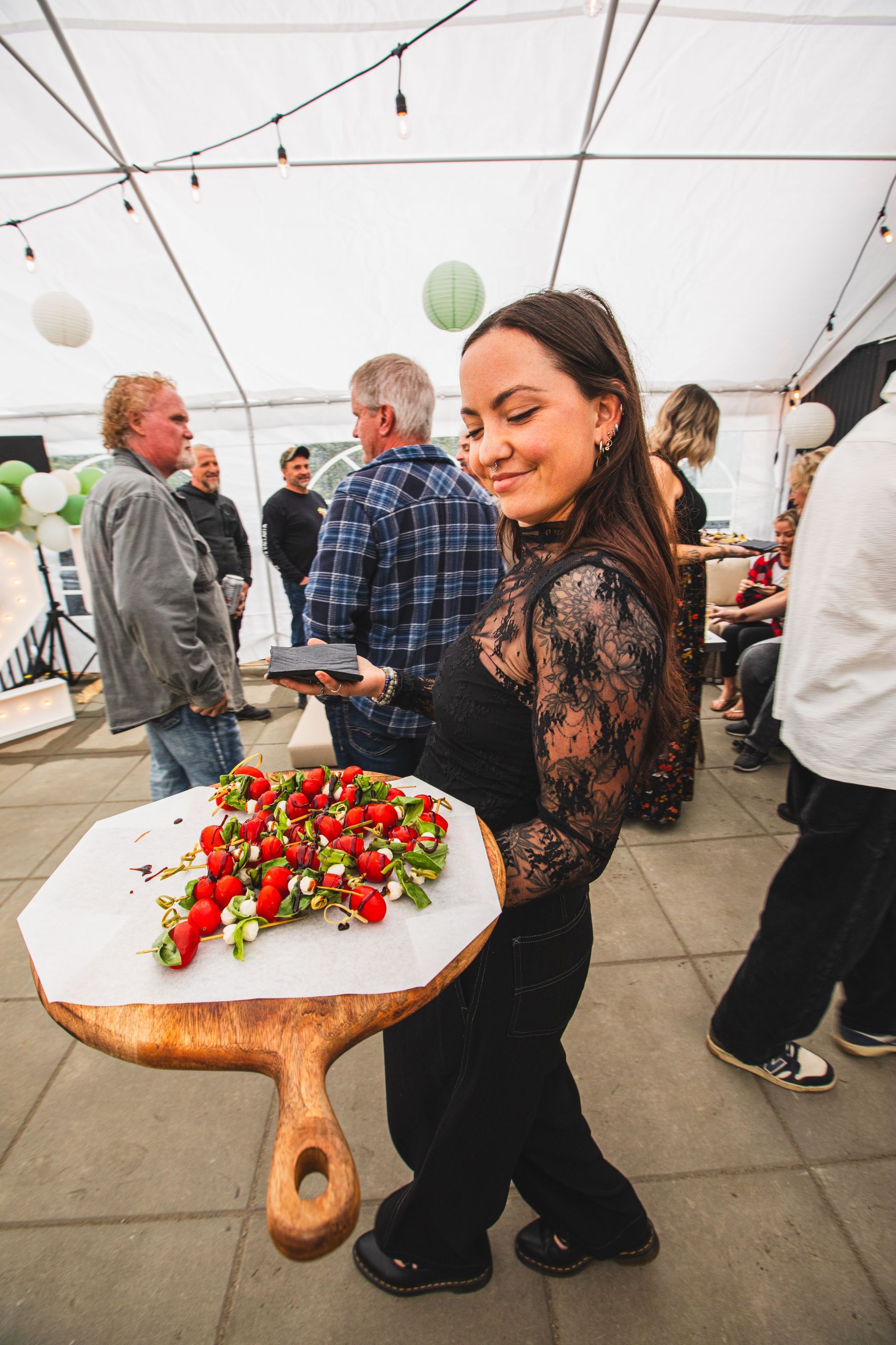A woman is holding a wooden cutting board with strawberries on it.