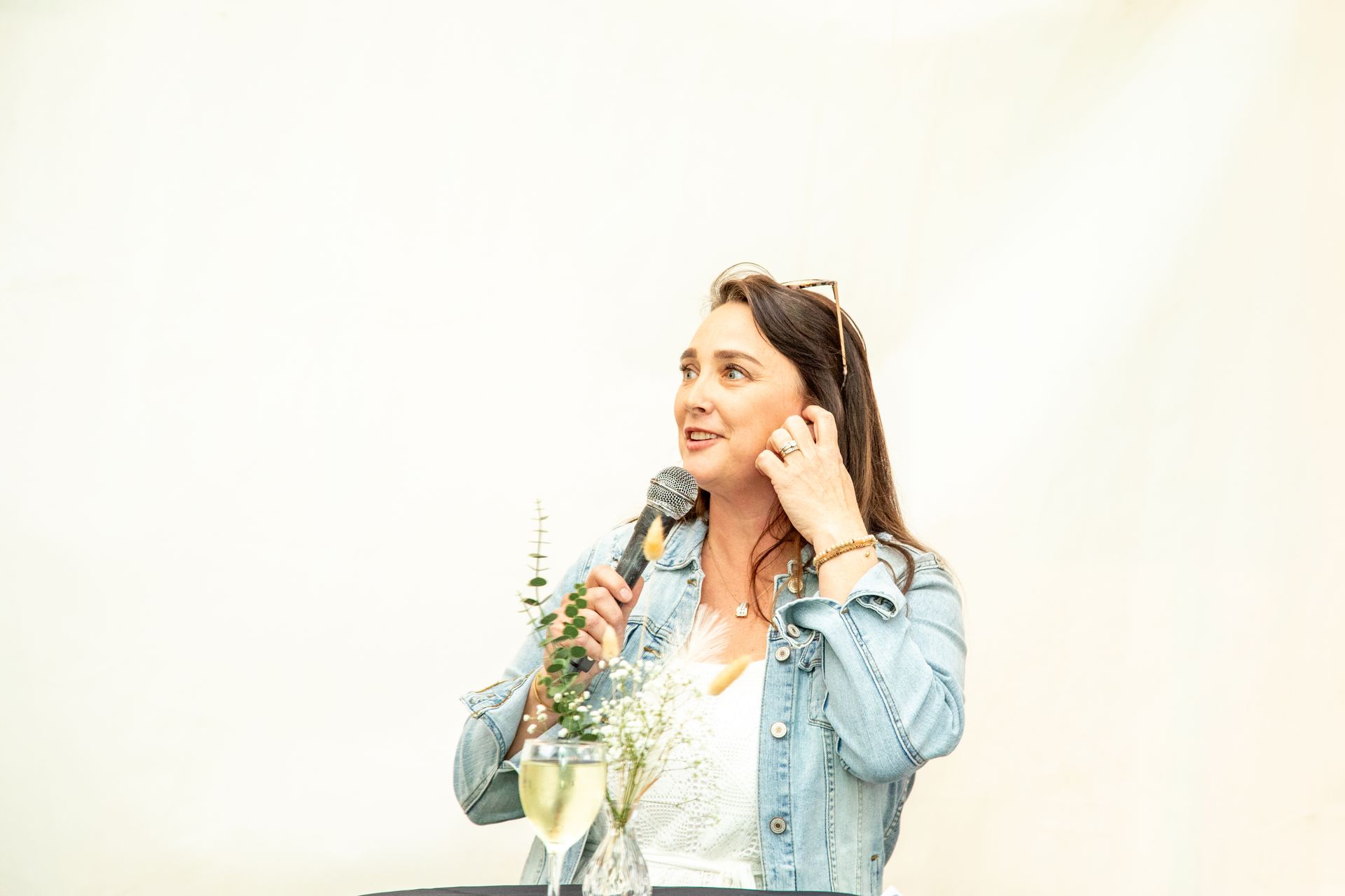 A woman is holding a microphone and a glass of wine.