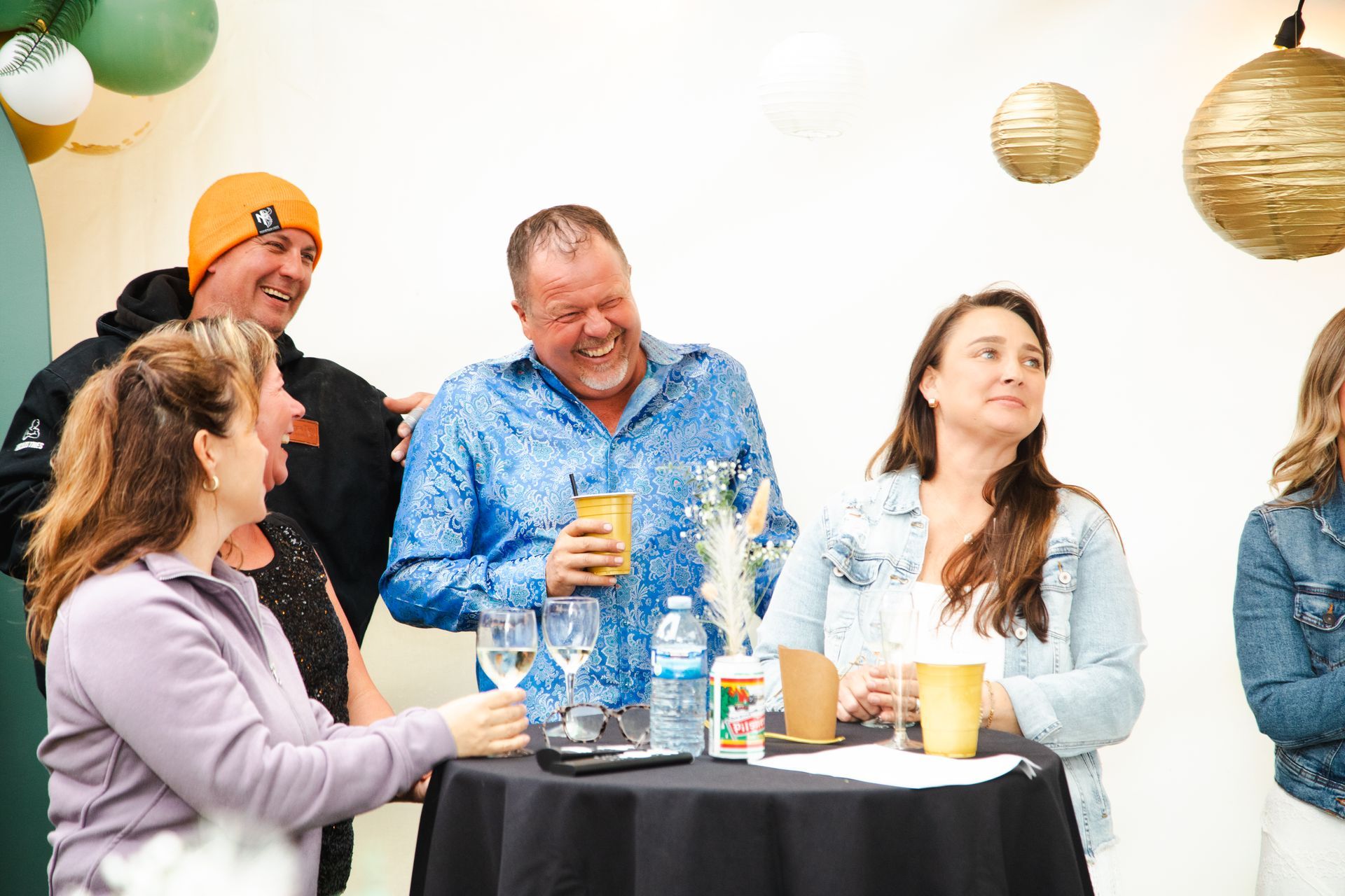 A group of people are sitting around a table laughing and drinking wine.