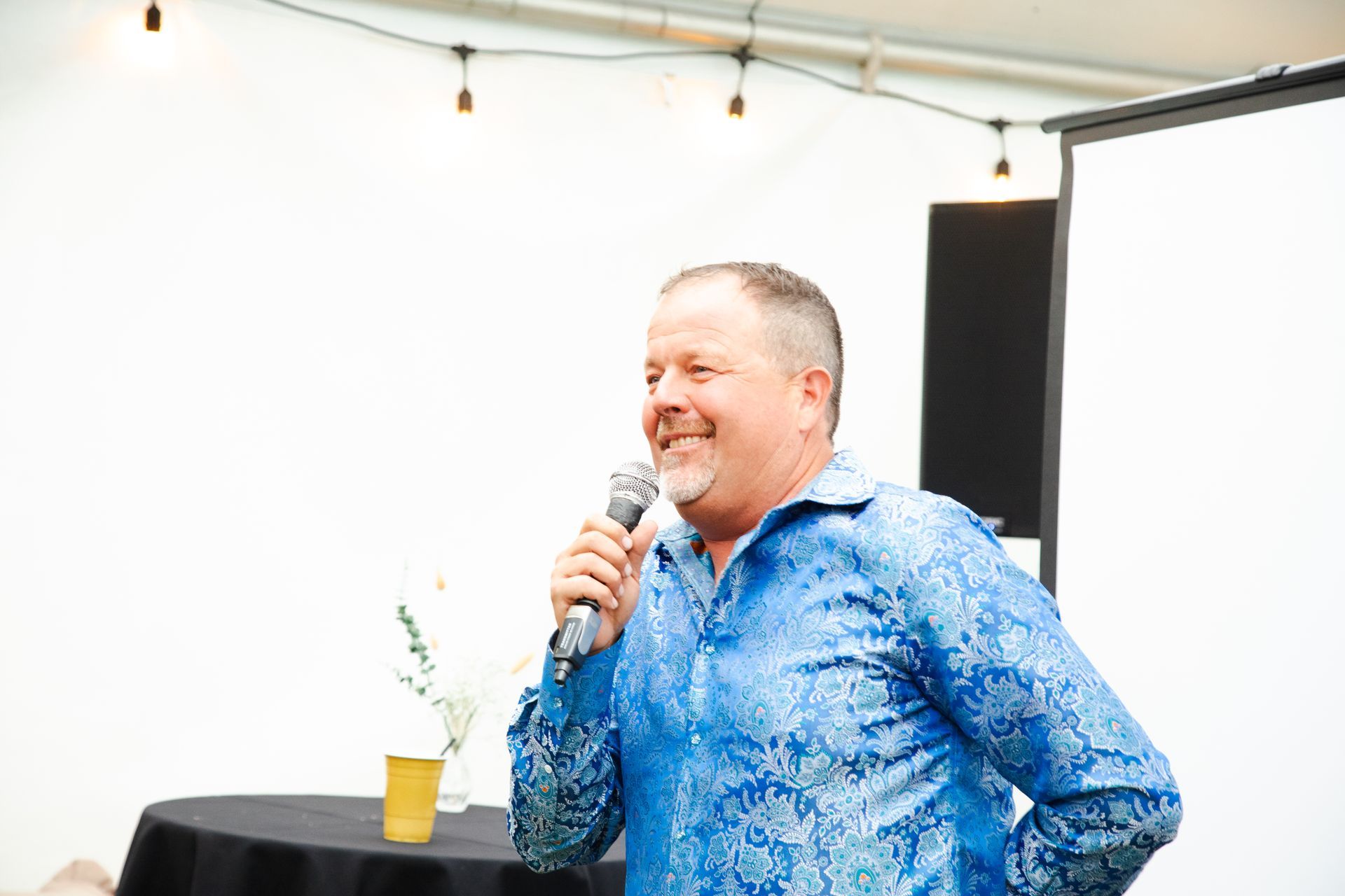 A man in a blue shirt is holding a microphone and smiling.