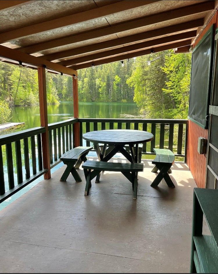 A porch with a picnic table and benches overlooking a lake