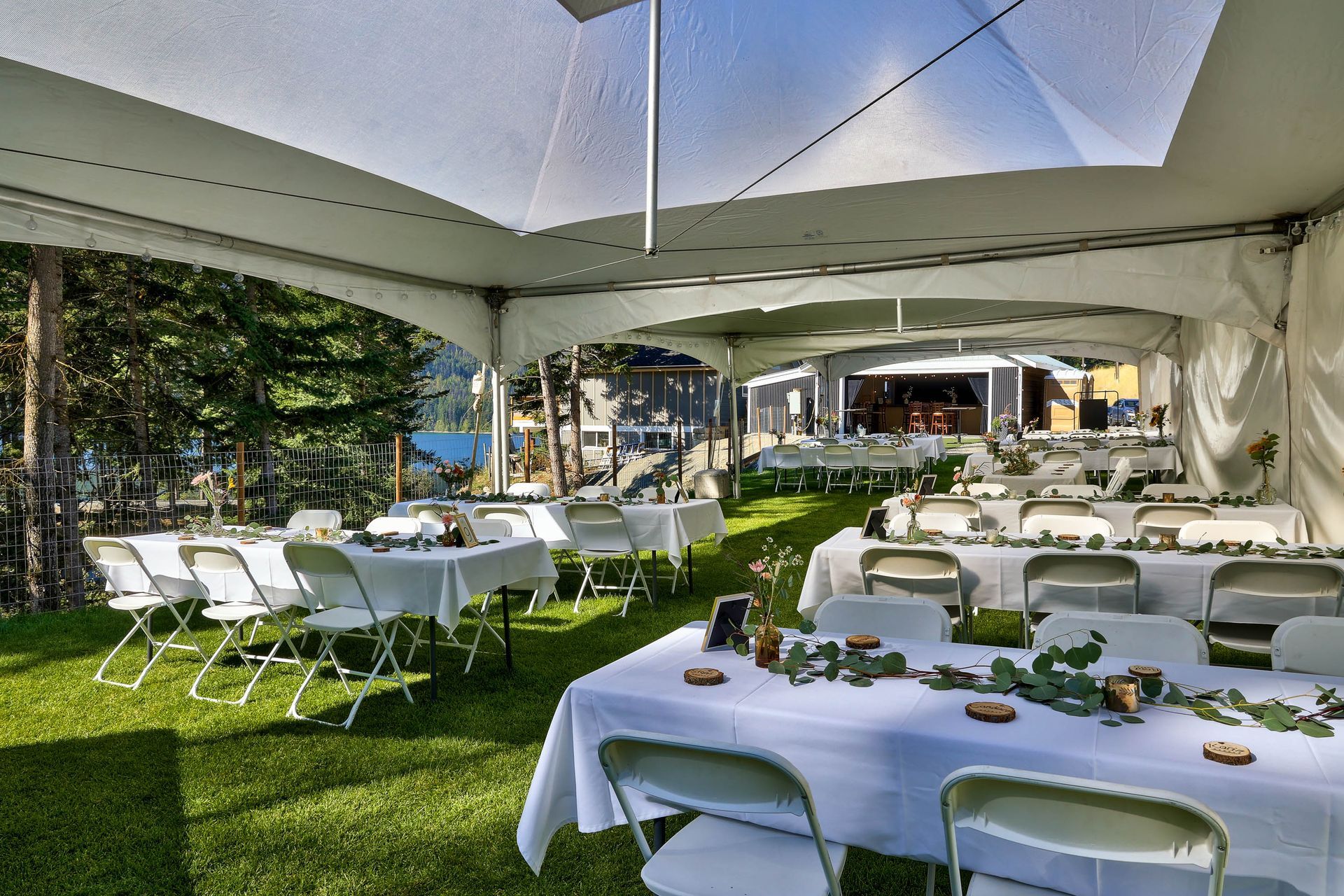 Tables and chairs are set up under a tent in the grass.