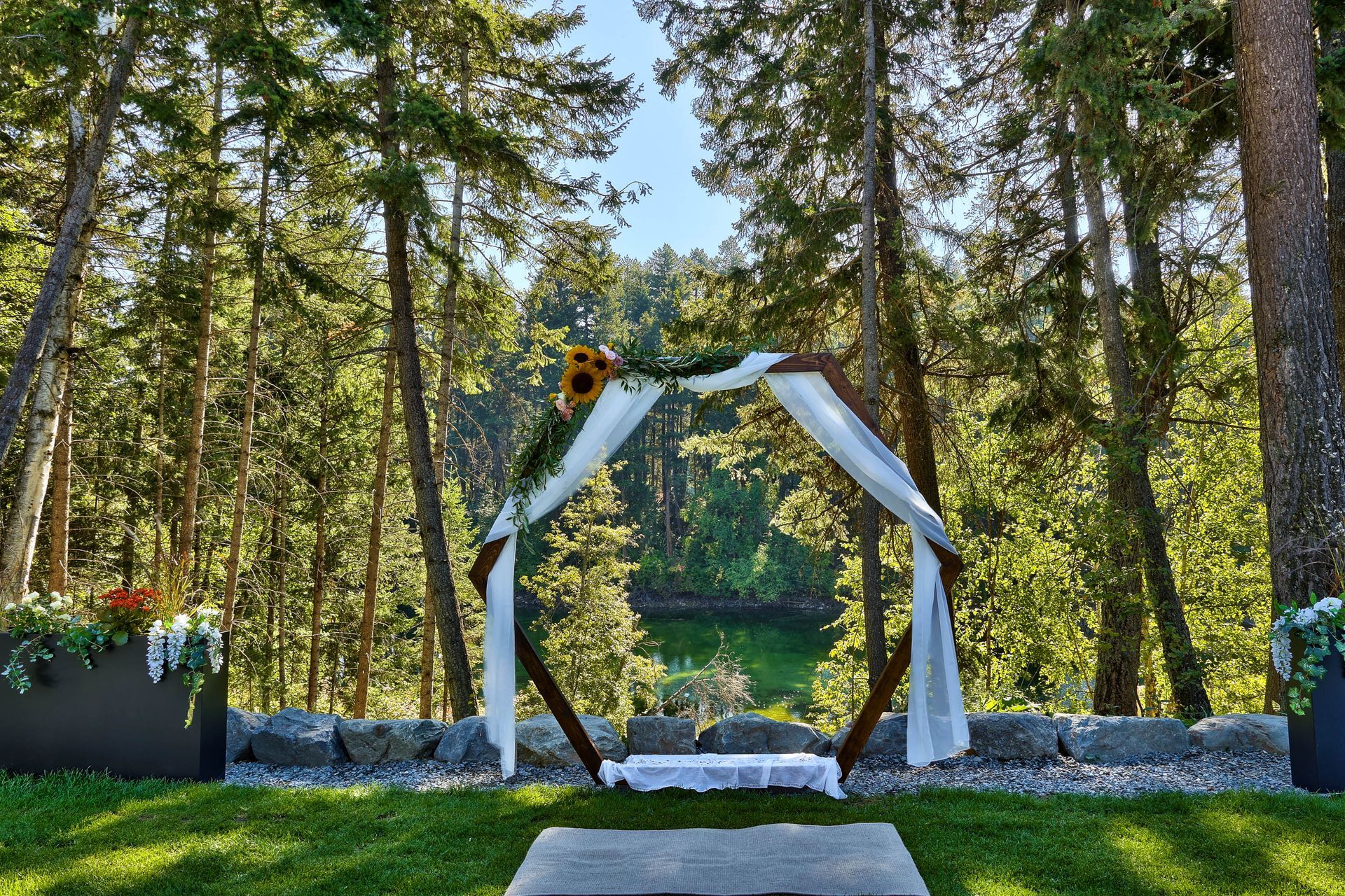 A wedding arch in the middle of a forest with a lake in the background.