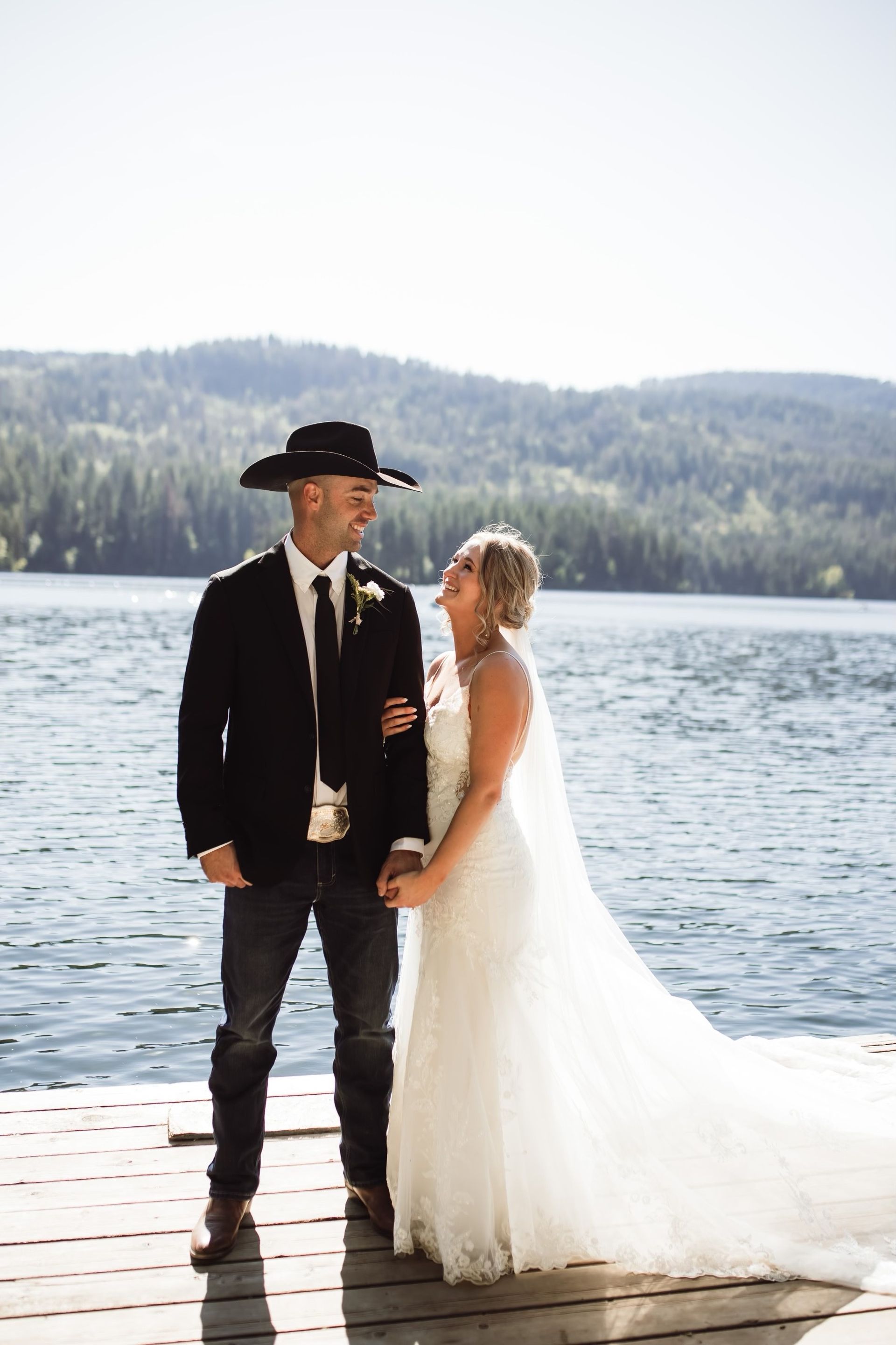 A bride and groom are standing on a dock next to a lake.
