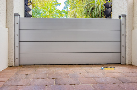 Gray flood barrier installed between pillars on a brick patio, protecting a doorway from water.