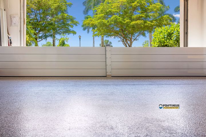 View through a doorway: Trees with green leaves and blue sky above a white barrier and light-colored floor.