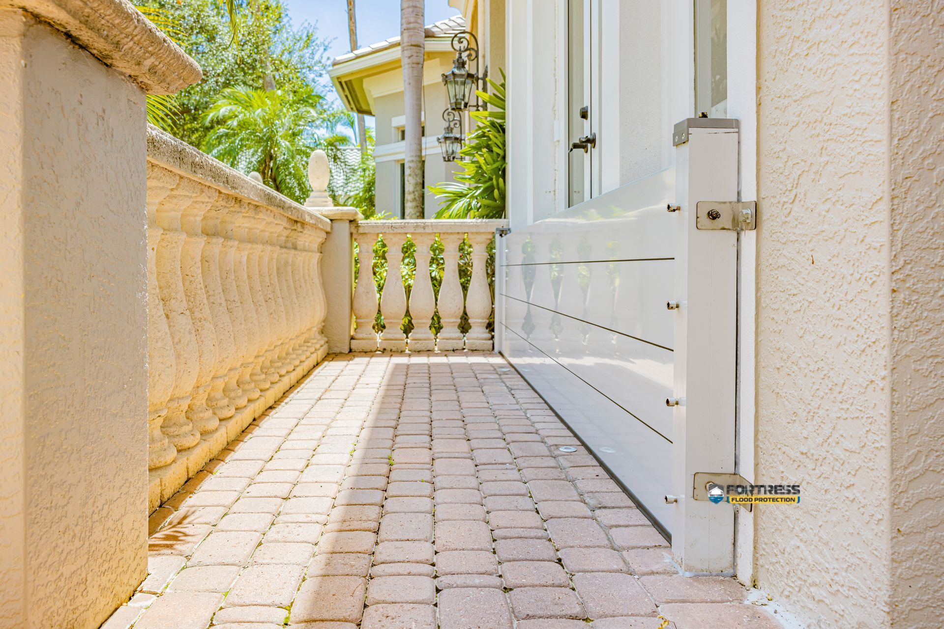 Brick patio with white flood barrier, ornate stone railing, and sunlight.