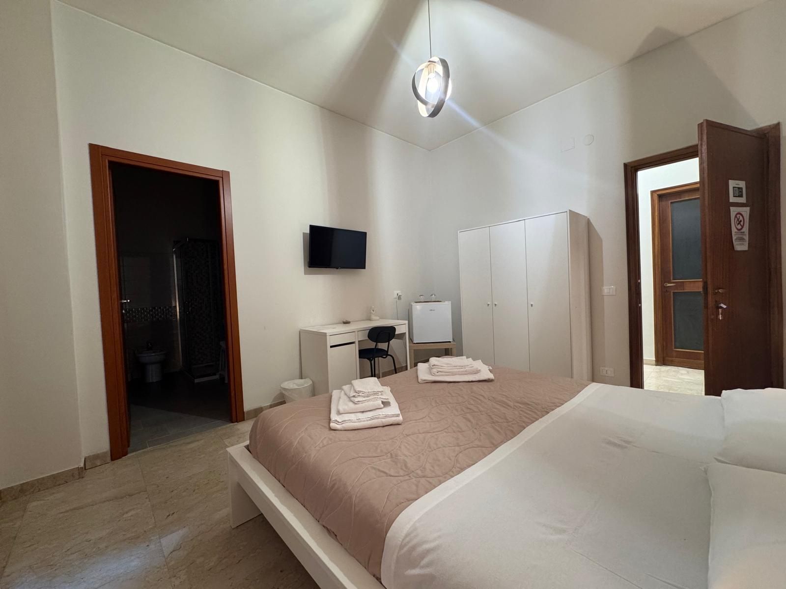 Una camera da letto con un letto grande, una scrivania, una televisione e una porta che conduce al bagno.