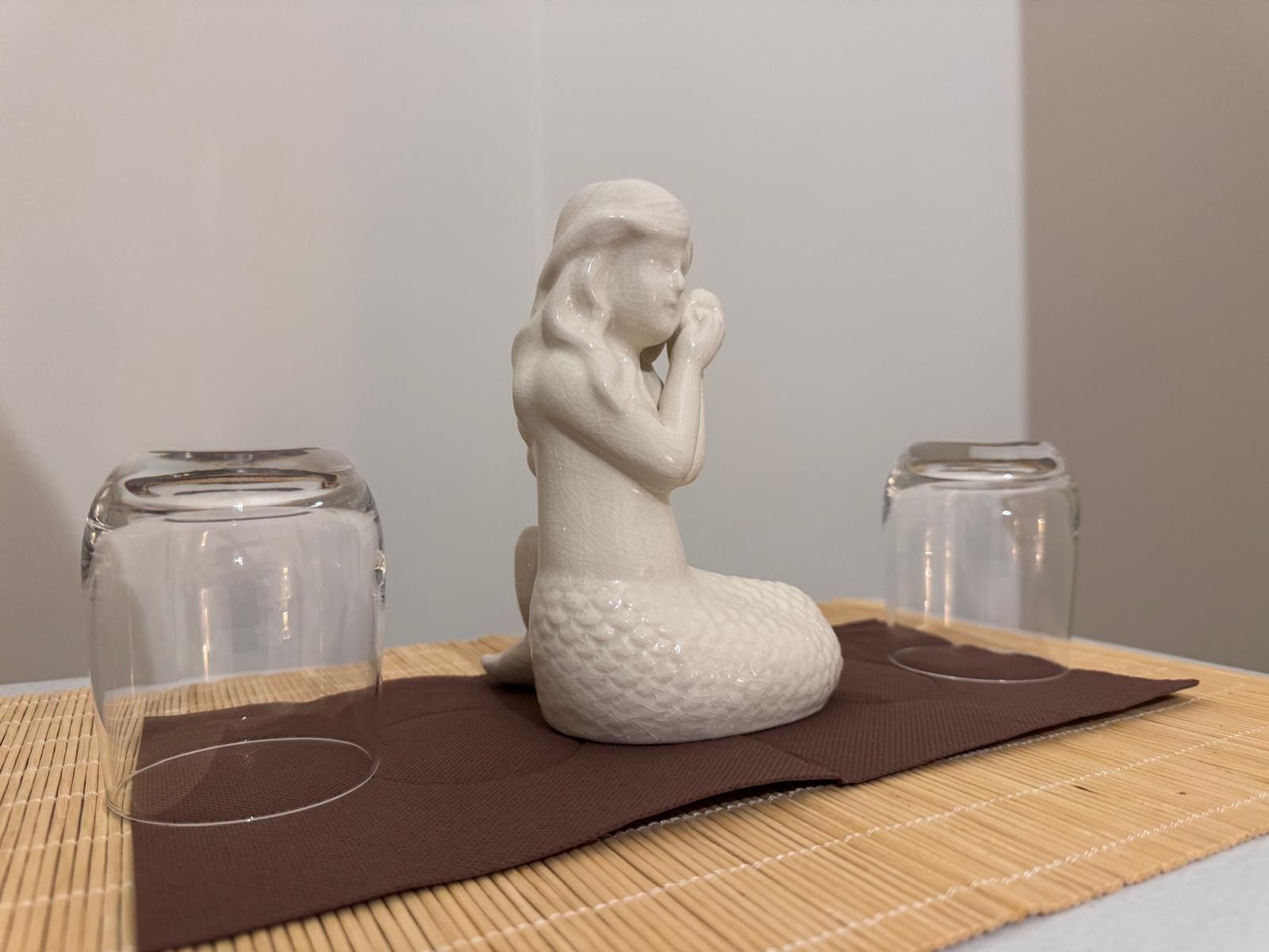 Una statua di una sirena è seduta su un tavolo accanto a due bicchieri.