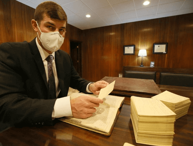 A man wearing a face mask is sitting at a table looking at a book.