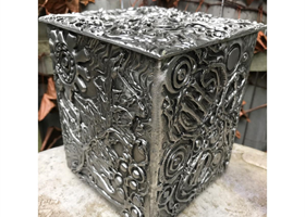 A silver urn with a pattern on it is sitting on a table.