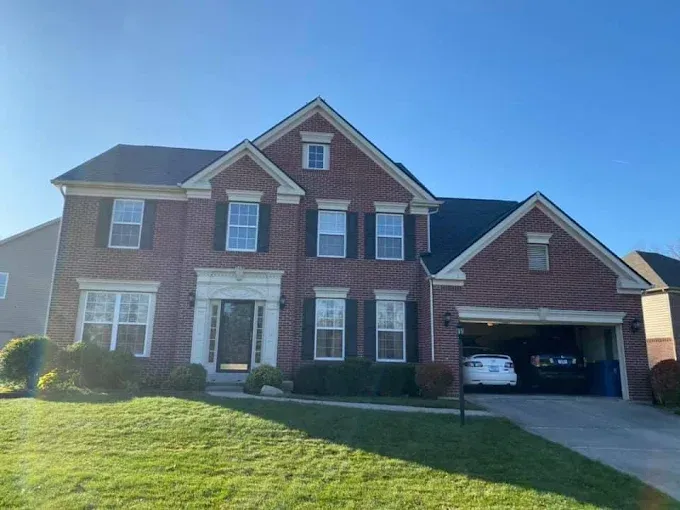 Brick two-story house with black shutters and a garage. Green lawn and a blue sky.