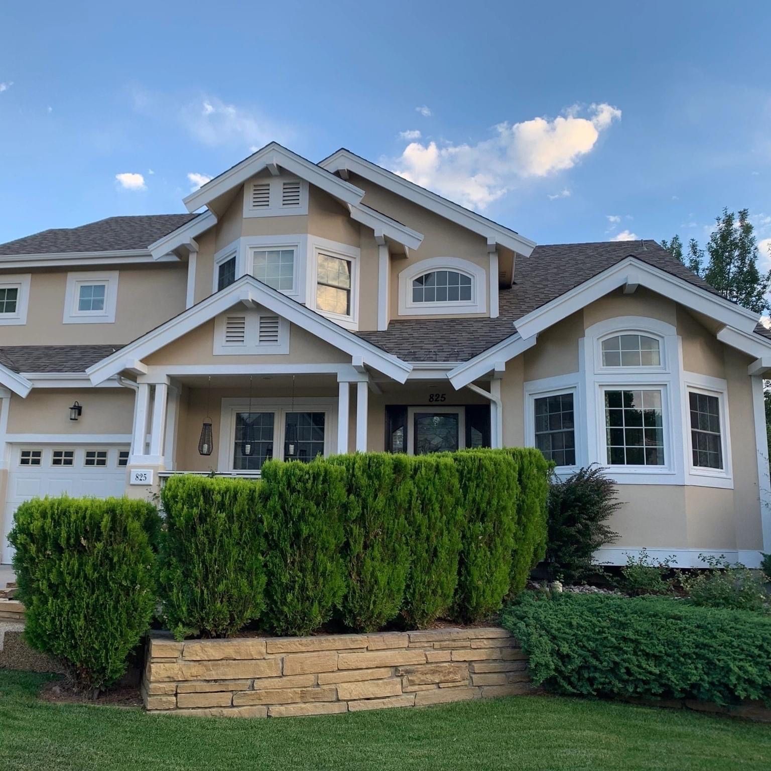 Brick two-story house with black shutters and a garage. Green lawn and a blue sky.