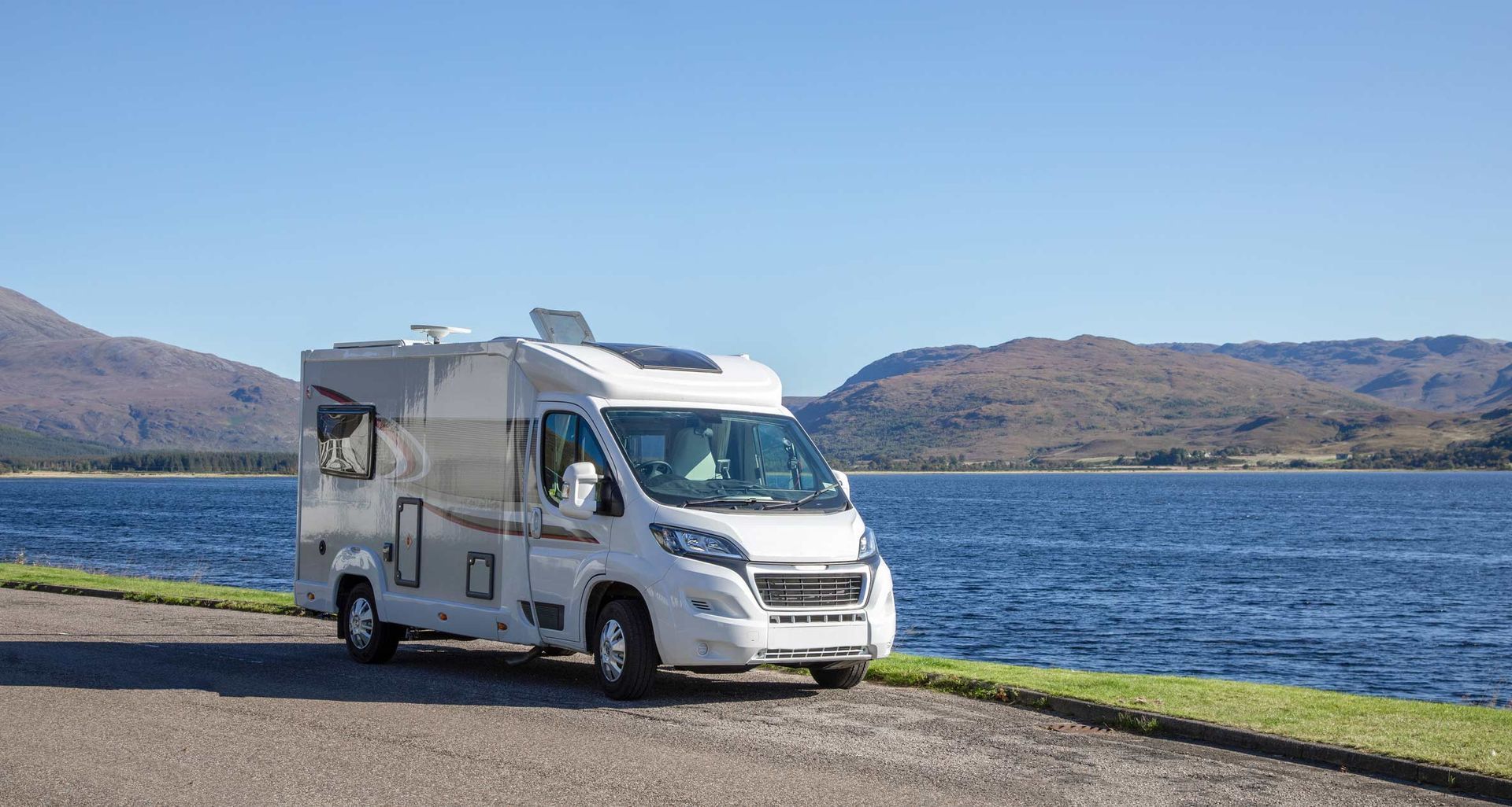 A white RV is parked next to a lake with mountains in the background