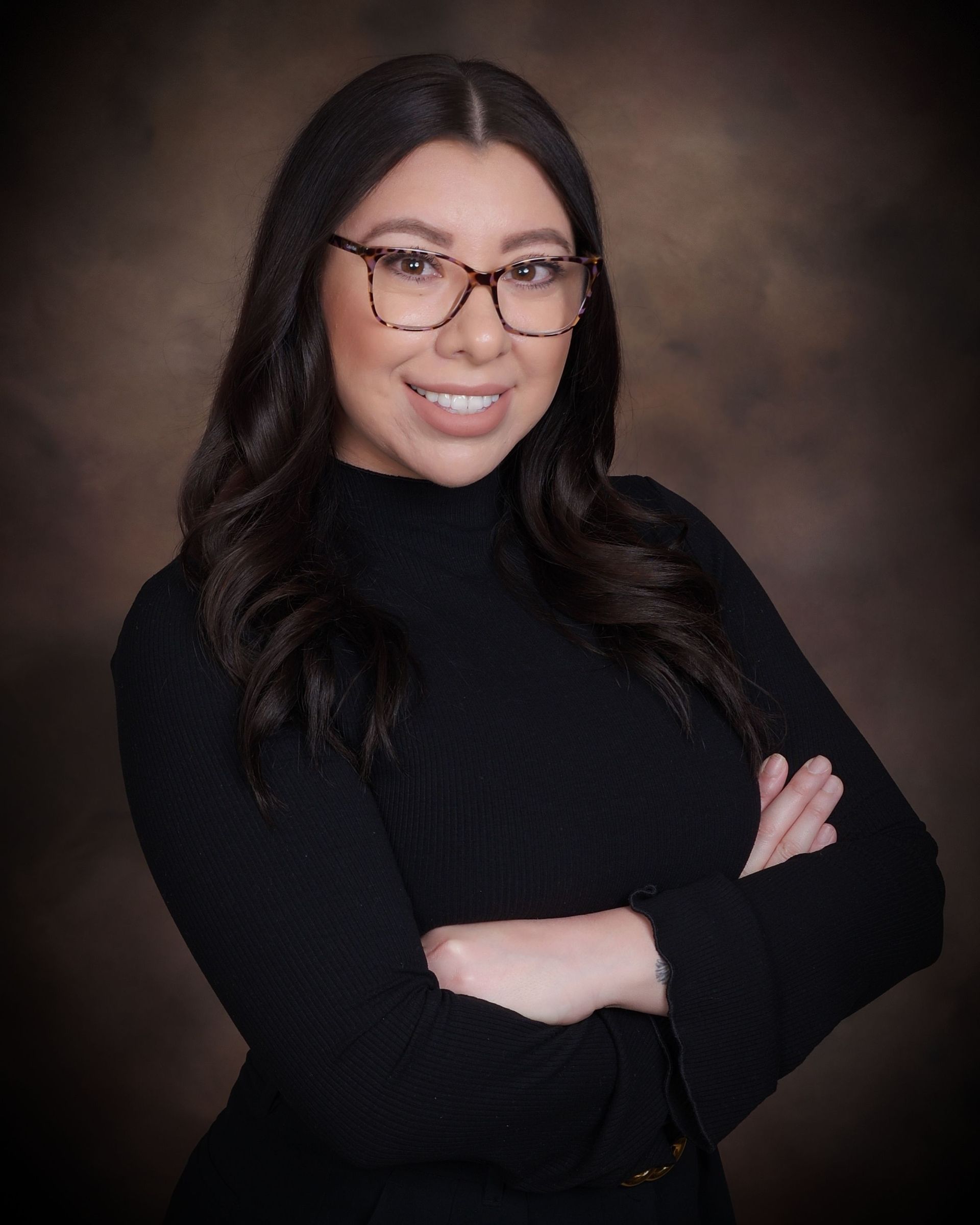 Woman in glasses, black turtleneck, arms crossed, smiling, studio background.